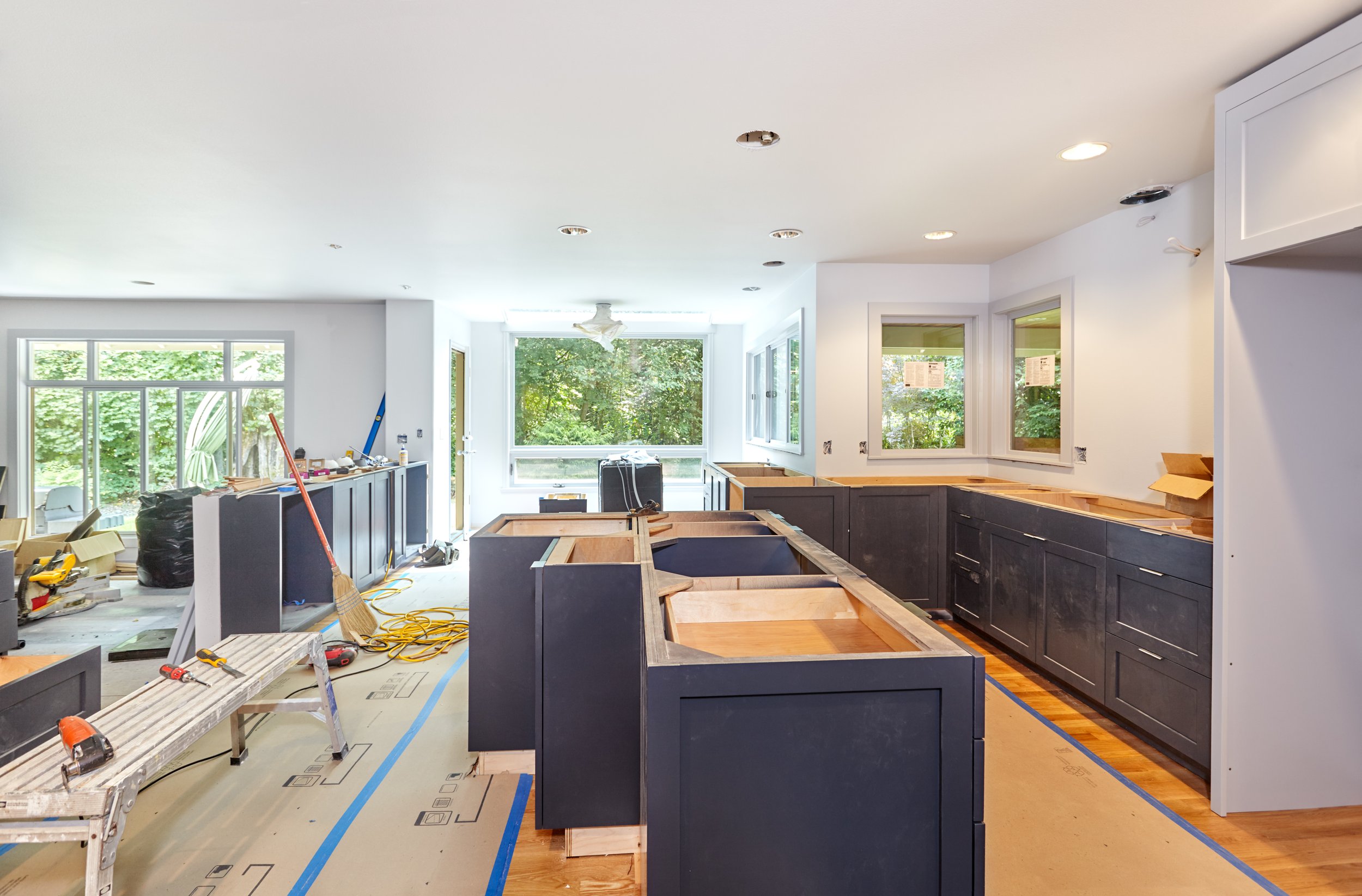 Kitchen under renovation with dark cabinets, countertops, and unfinished surfaces, construction tools, and protective floor covering.