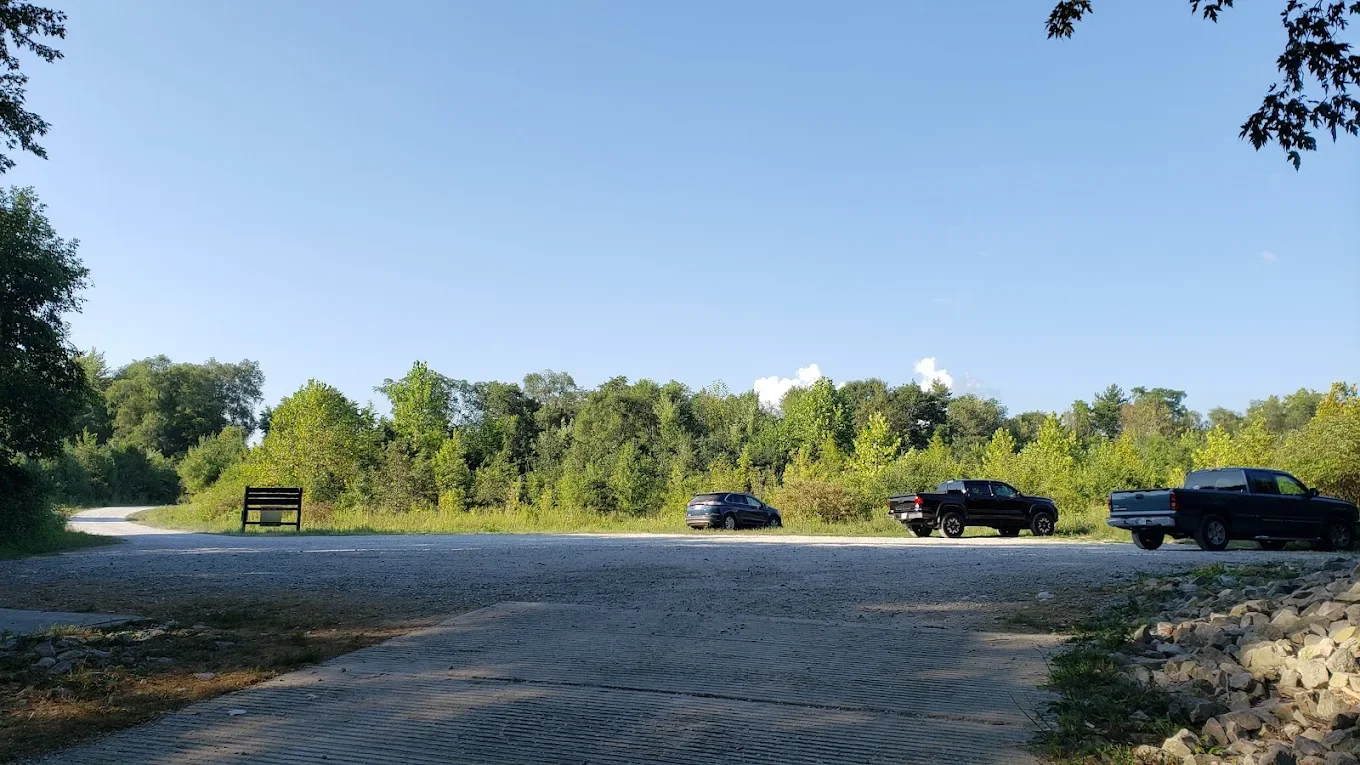 Three black pickup trucks parked on the side of a gravel road at a wooded area under a clear blue sky.