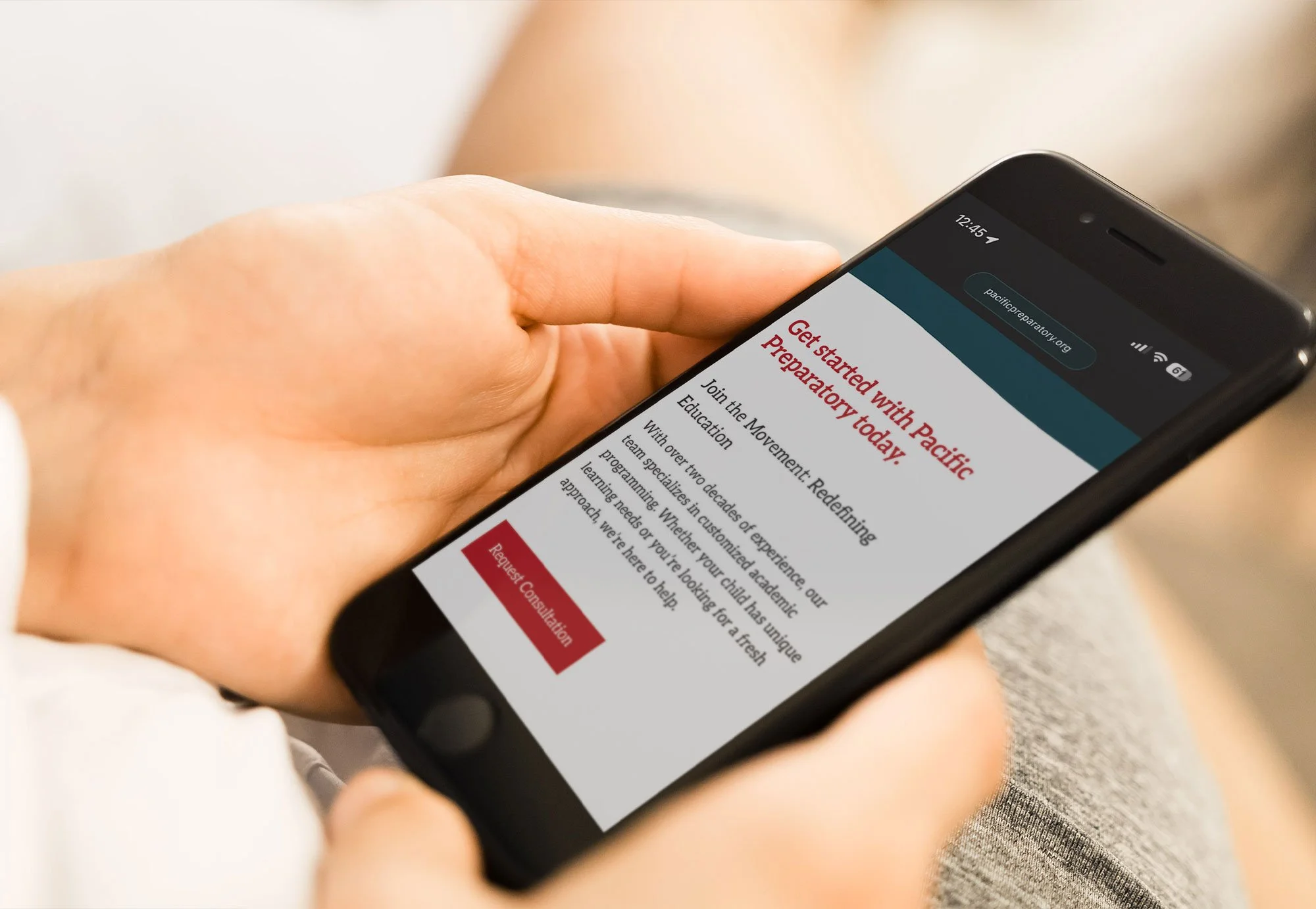 A person holding a smartphone displaying a webpage for Pacific Preparator, encouraging to get started with their preparatory education, with a 'Request Consultation' button visible.
