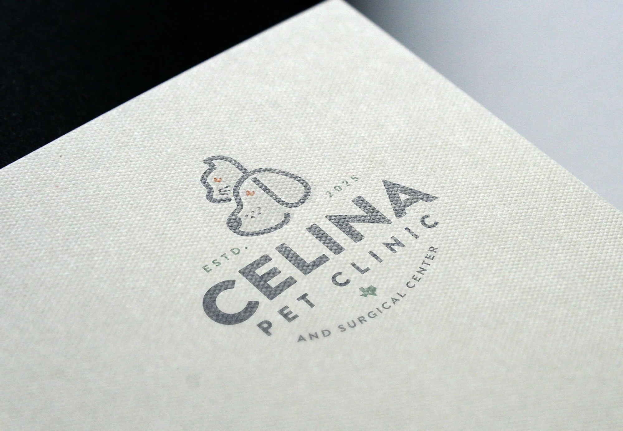 Close-up view of a textured paper with a logo for Celine Pet Clinic featuring a simple line drawing of a dog and a cat, with text indicating the clinic is established and includes an orthopedic theme.