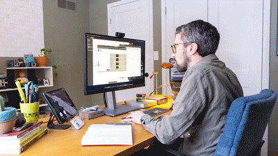 A man working at a desk with a computer monitor, tablet, and office supplies in a home office.