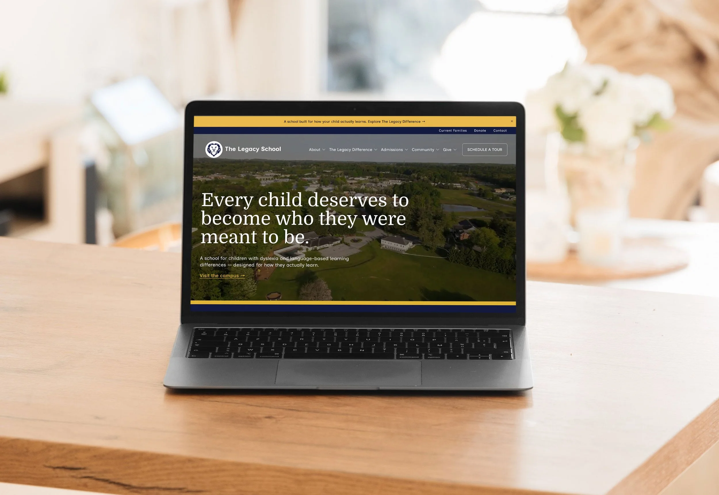 Laptop on a wooden table displaying a website for The Legacy School with the slogan "Every child deserves to become who they were meant to be," featuring an aerial view of a school campus and a menu bar at the top.
