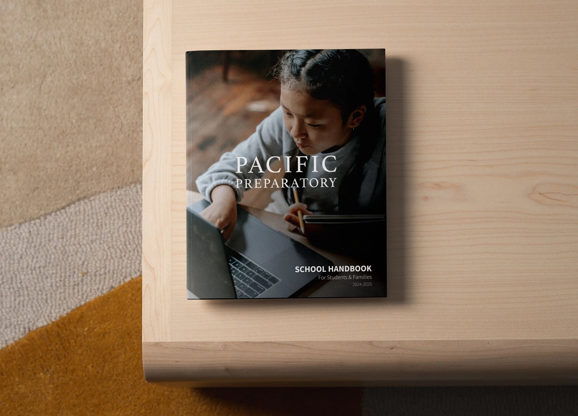 School handbook for students and families titled 'Pacific Preparatory', with a cover photo of a young person working on a laptop, placed on a light wooden table.