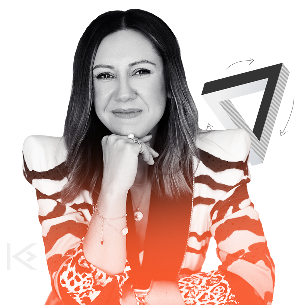 Kate Dillon with shoulder-length hair wearing a lion-patterned blazer, holding her chin with one hand, looking at the camera.