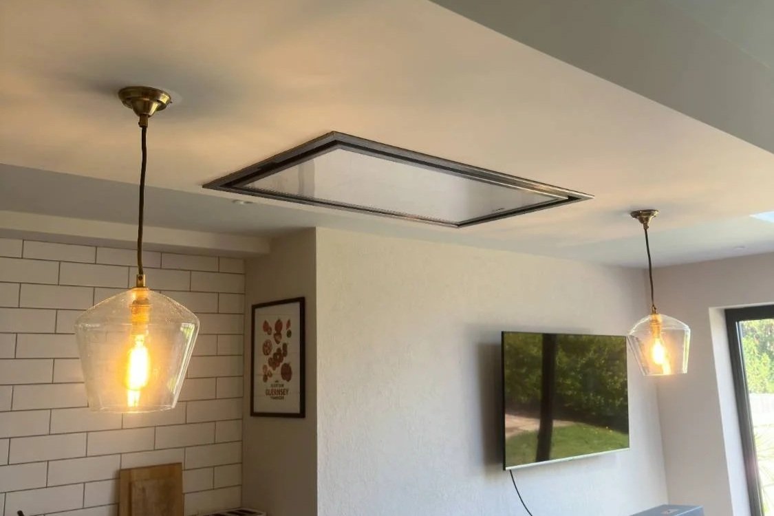 Living room with two hanging pendant lights, a flat-screen TV on a white wall, a framed art print, and a window showing trees outside.