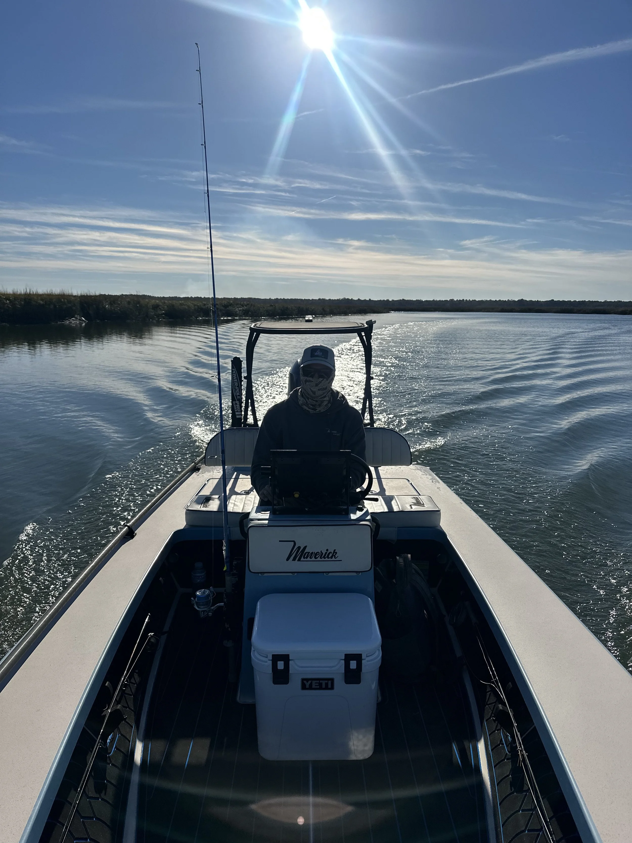 Person operating a boat on a calm lake under a bright, sunny sky with scattered clouds.