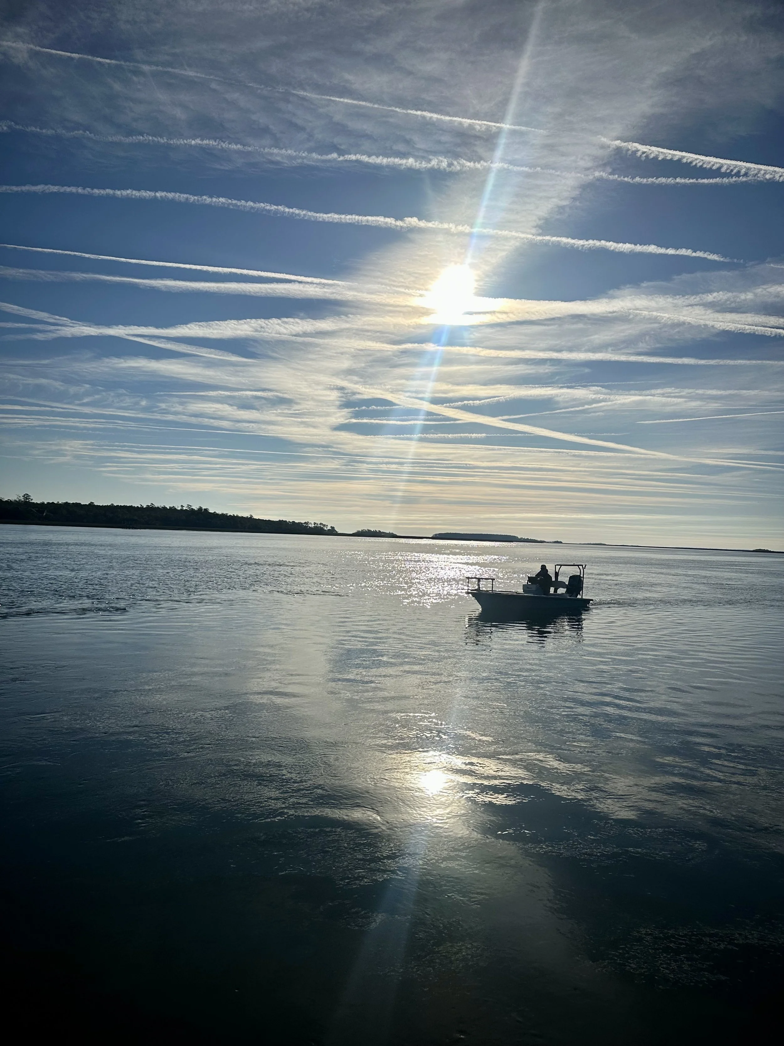 Serene landscape of a calm river with a boat, lush green grass in the foreground, and a sky with scattered clouds during sunset or sunrise.