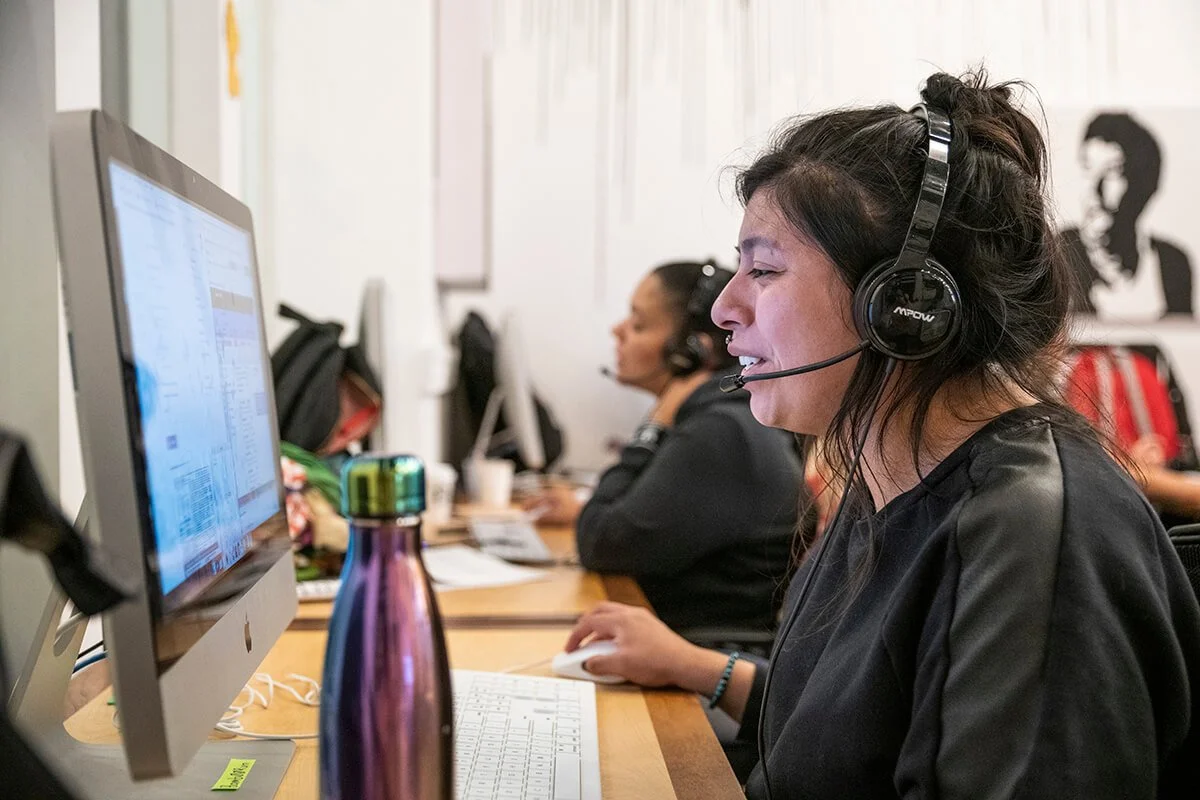 Woman wearing headphones and speaking to someone while typing on computer