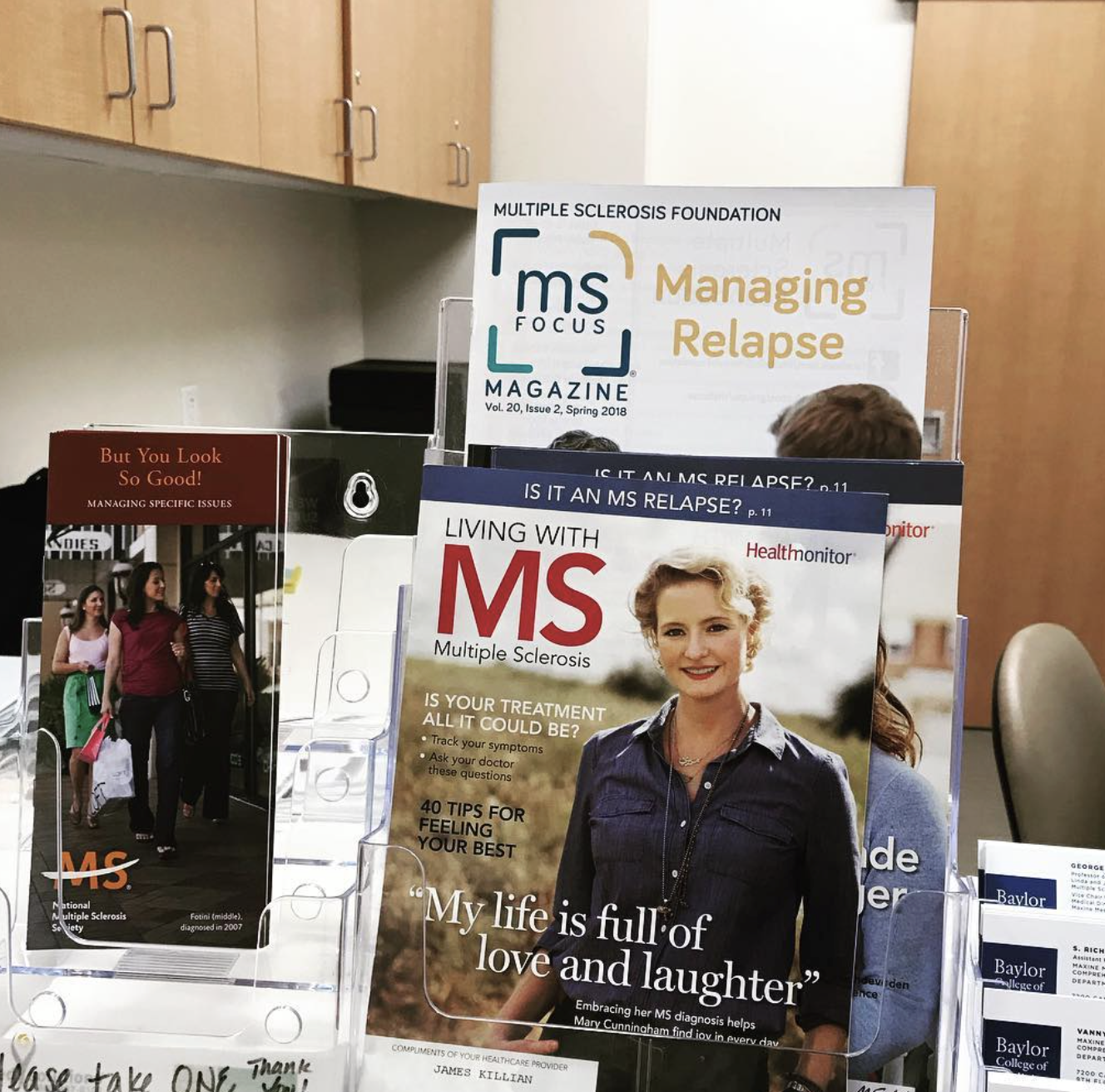 A selection of magazines featured at Maxine Mesinger Multiple Sclerosis Clinic, foremost is the MS edition of Health Monitor with Mary Joan Cunningham featured on the cover. The headline says, "My life is filled with love and laughter