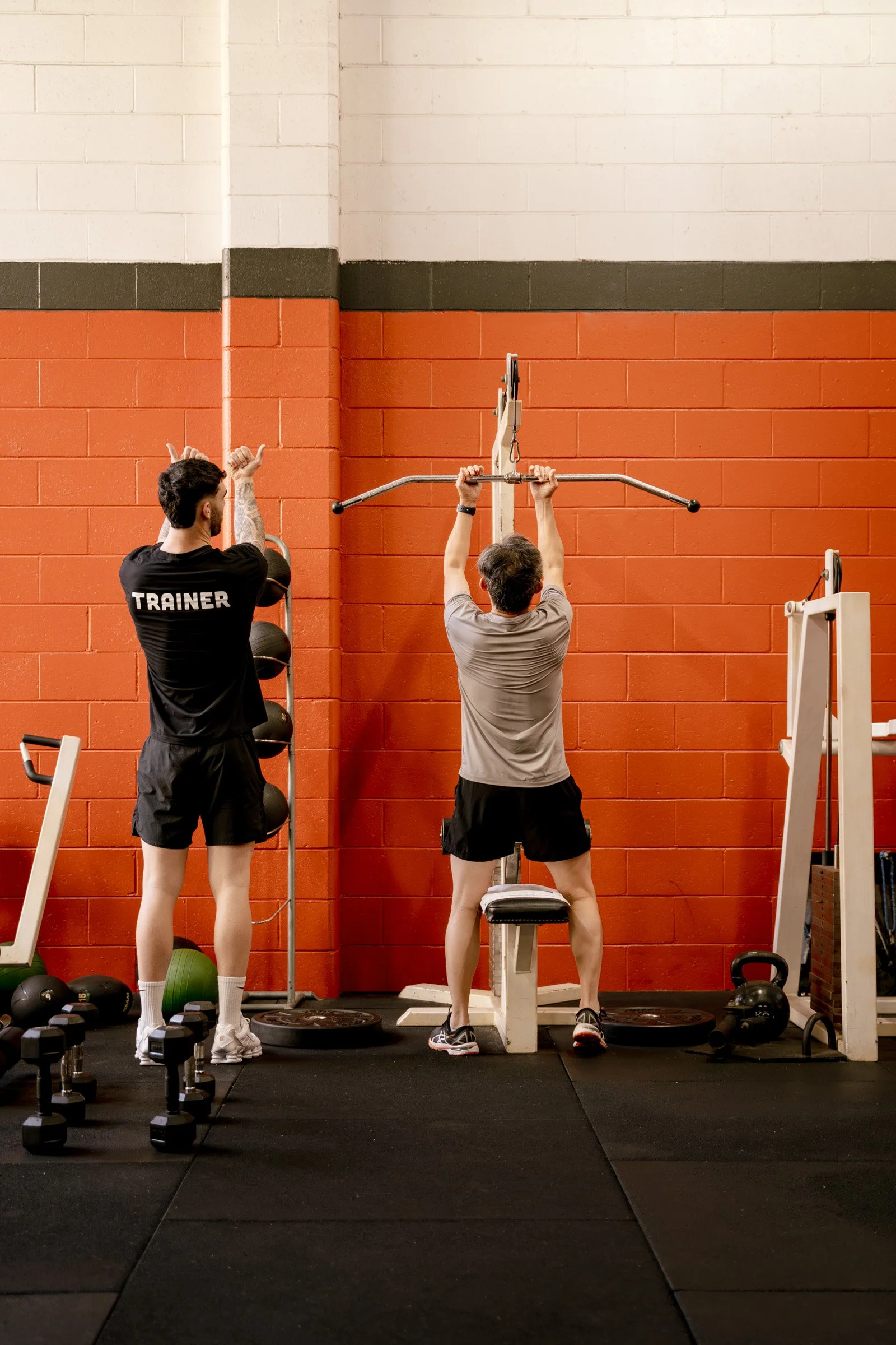 A personal trainer instructs a woman during her workout in a gym, with the woman lifting a barbell.