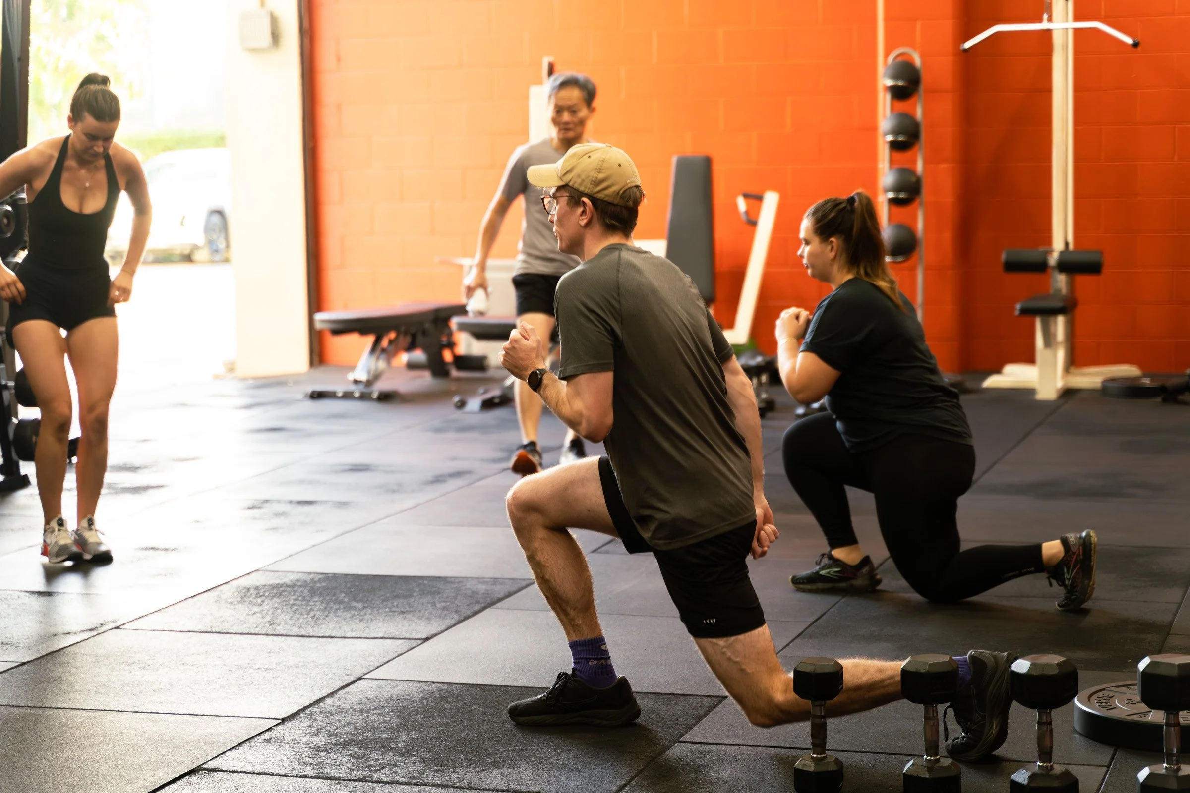 Woman in black t-shirt and gray shorts doing a medicine ball overhead in a gym.