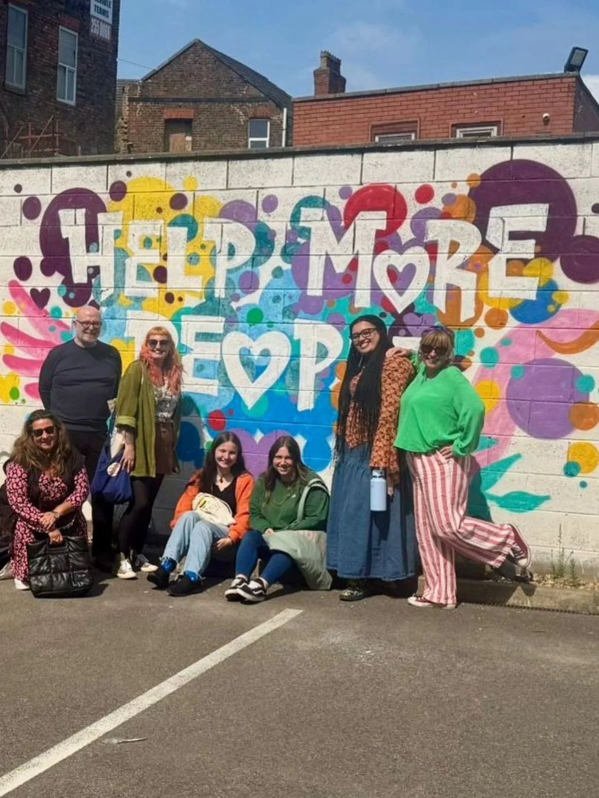 Group standing in front of a “Help More Hope” mural—community impact and optimism.