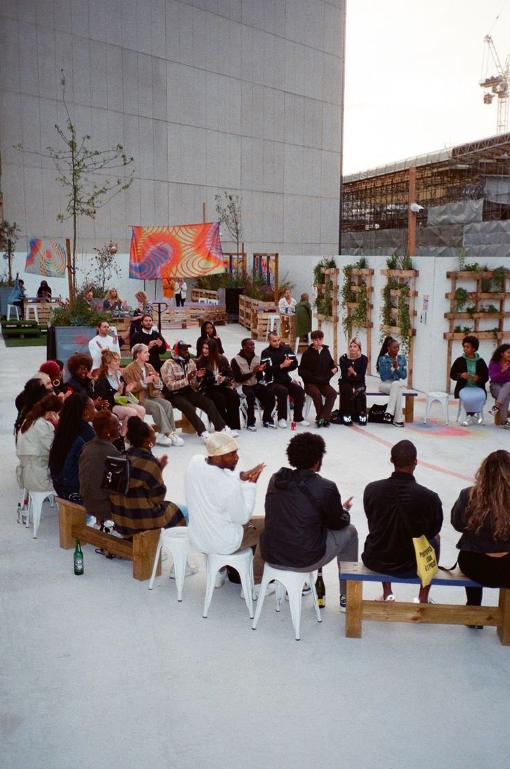 People gathered in an outdoor circle, clapping and listening—community-led engagement and facilitation.