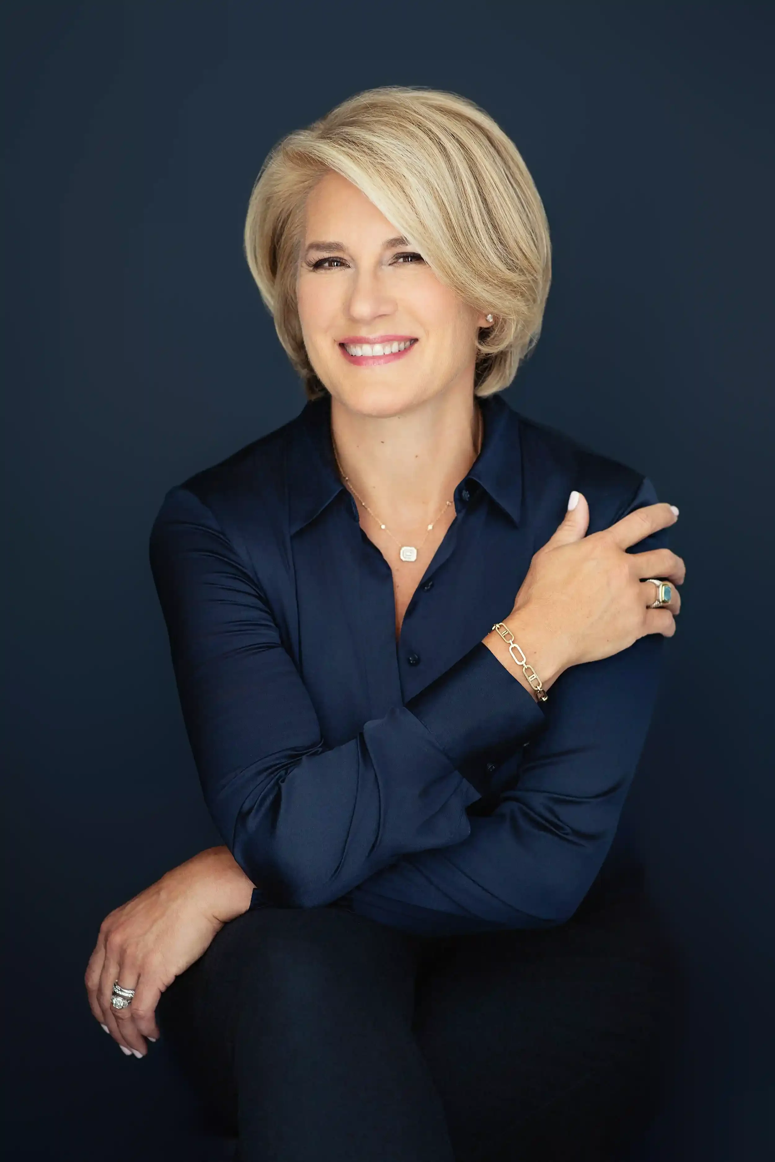 Ivy Horan, gift consultant, poses against a dark blue background, wearing a dark blue satin blouse and jewelry