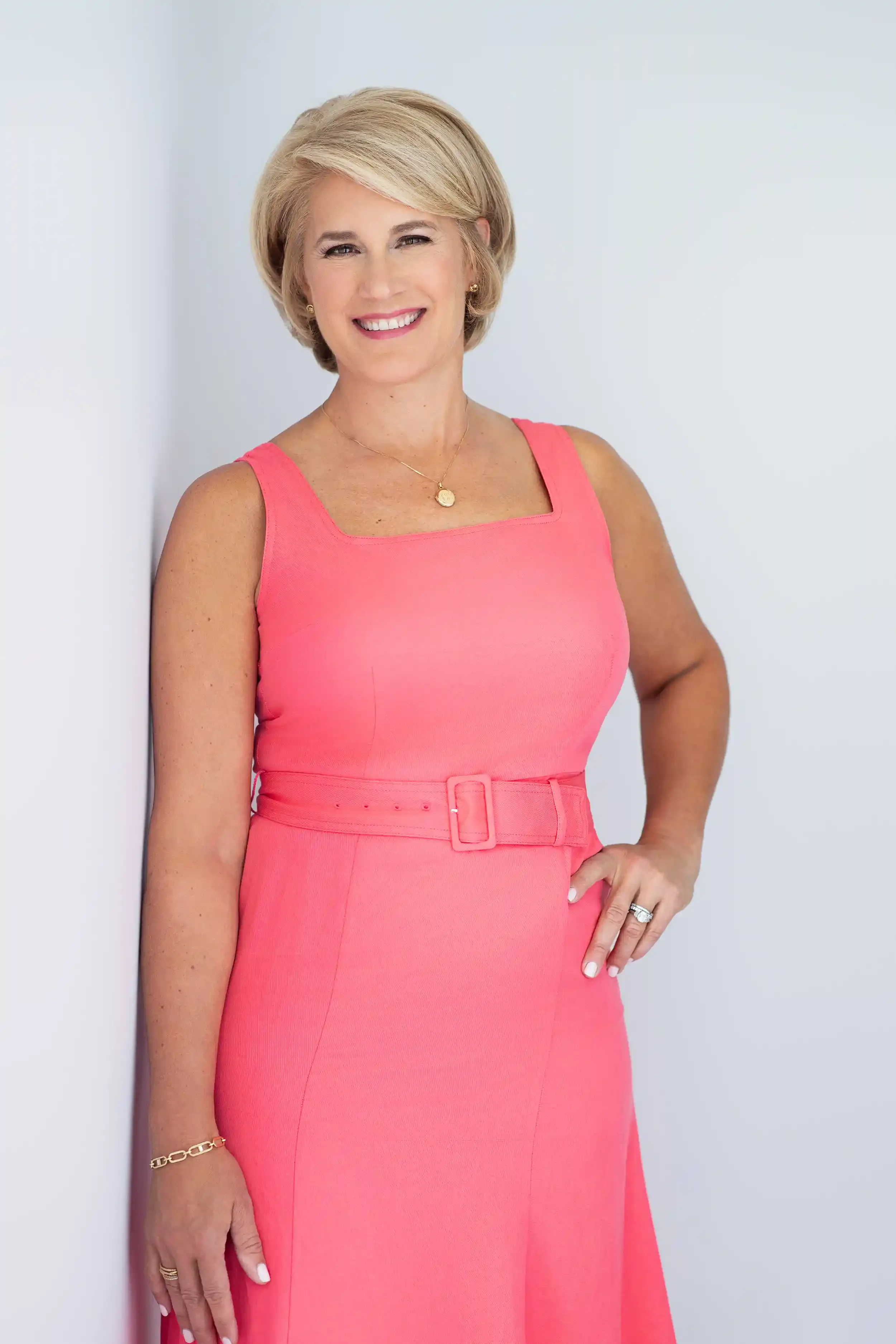 Ivy Horan, gift consultant, wearing a pink sleeveless dress with a belt, smiling and standing with one hand on her hip