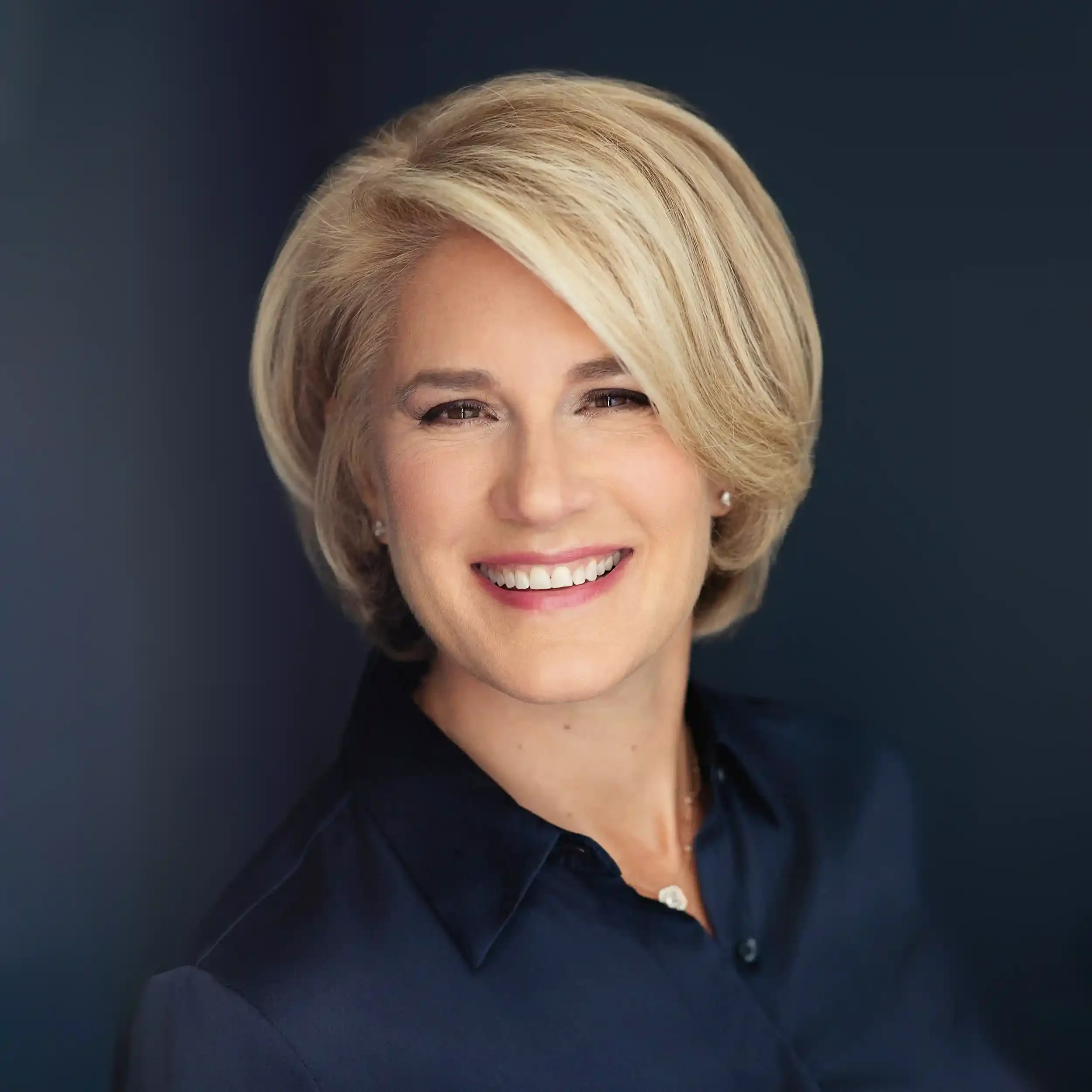 Ivy Horna, gift consultant, smiling, wearing a dark blue collared shirt, against a dark blue background