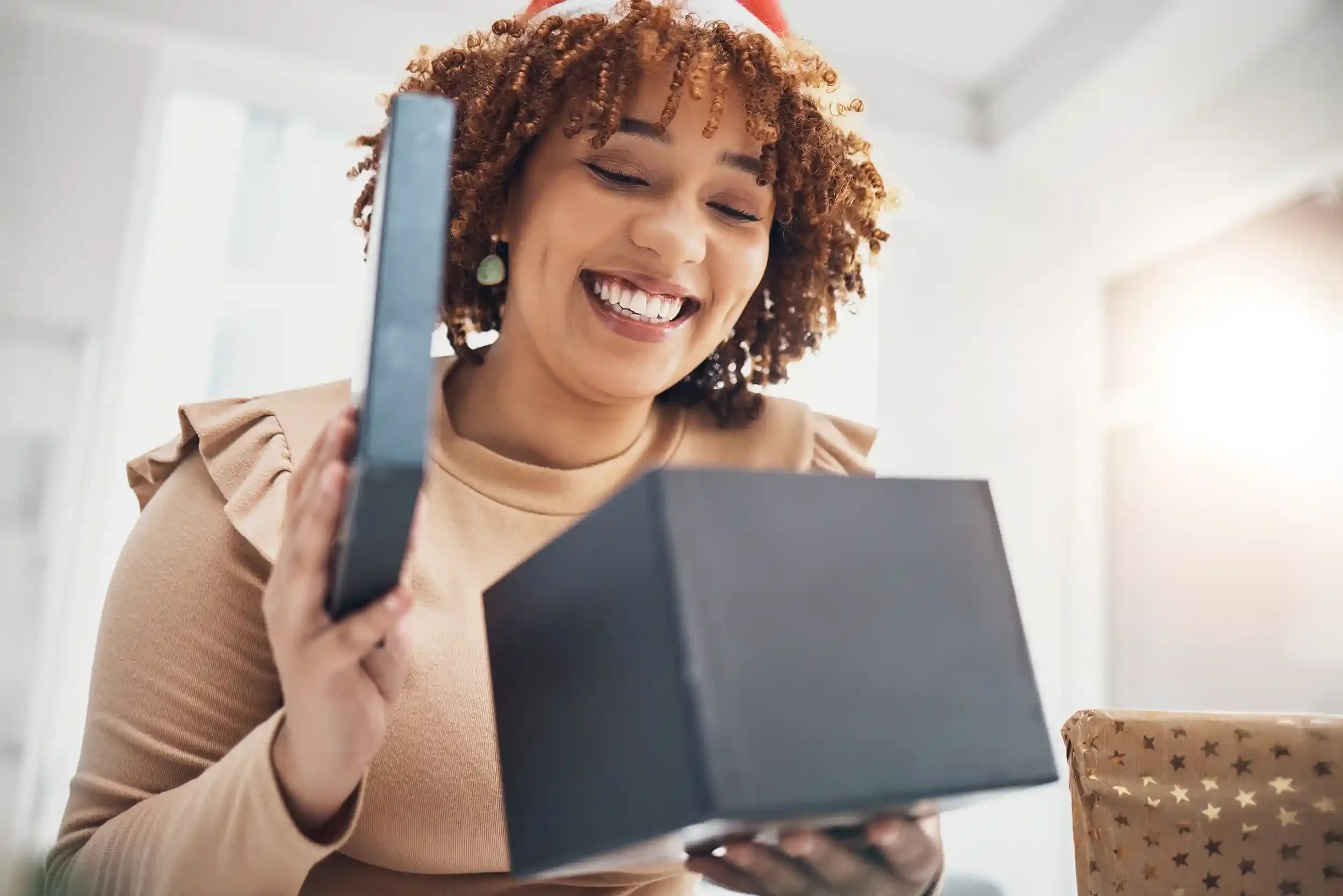 A woman opening a gift box with a smile, holding a small black box and a card