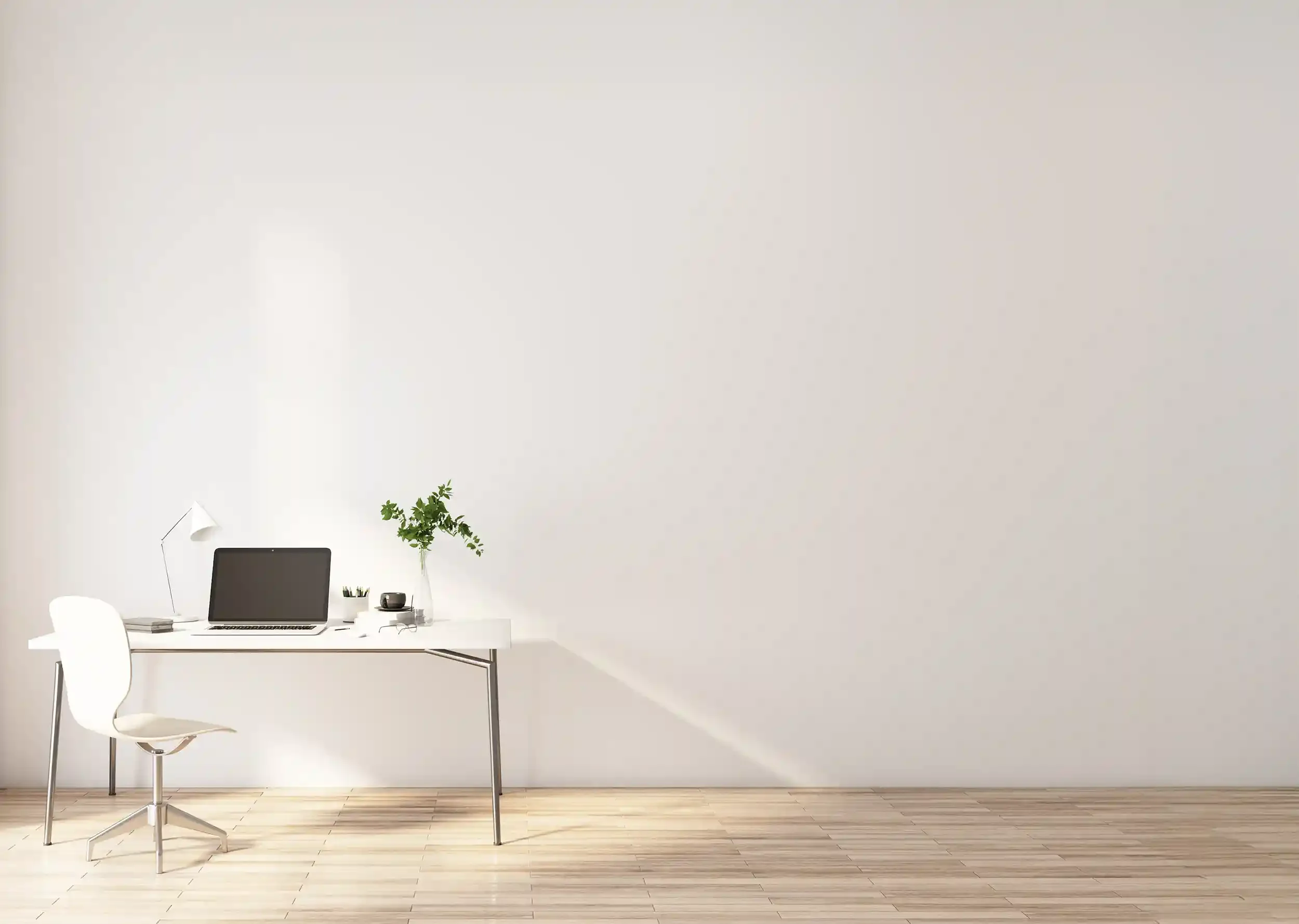 Minimalist office with white wall, white desk, white chair, laptop, desk lamp, plant, and small decor items on a light wood floor