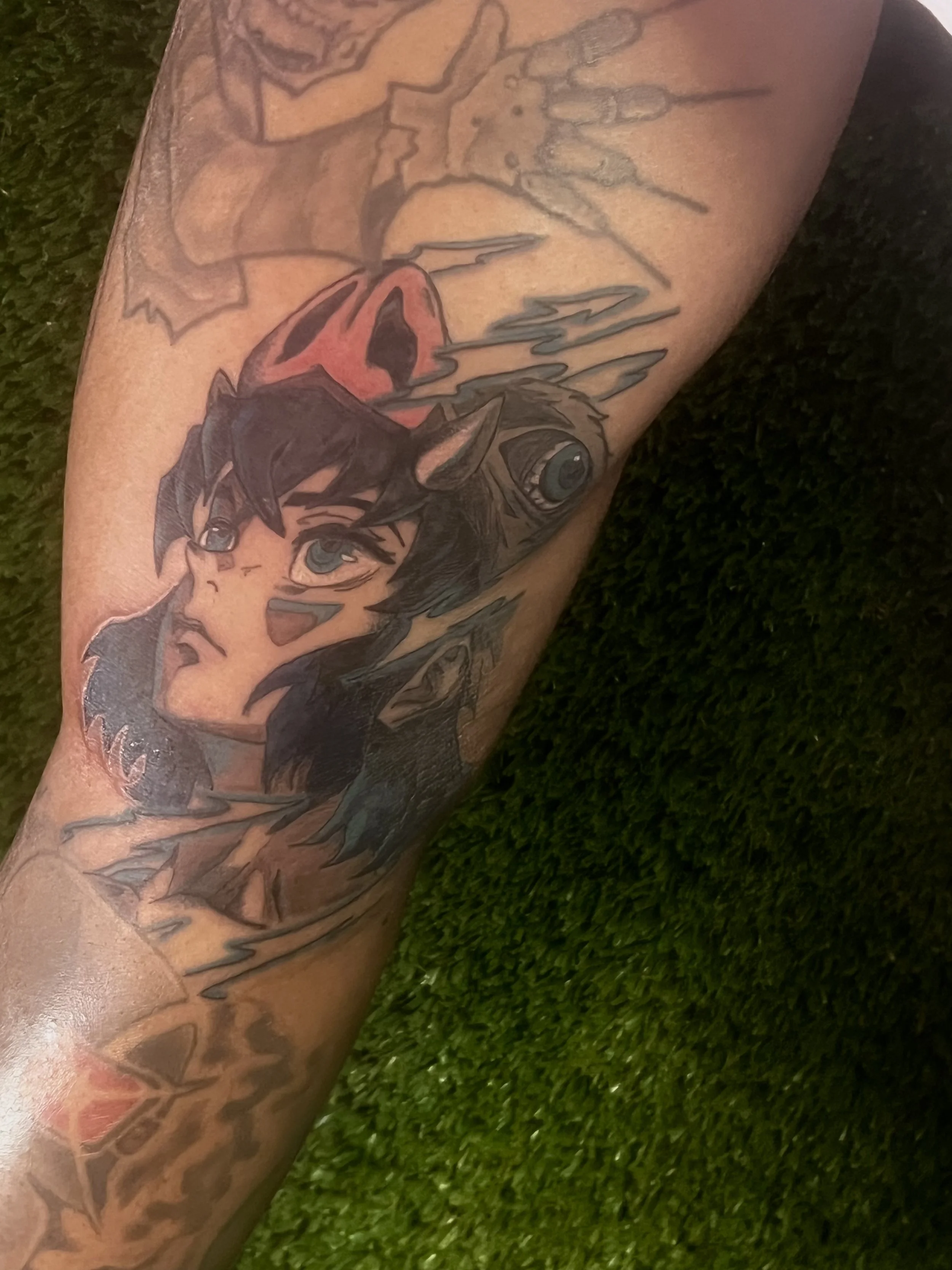 Tattoo of Inoske from Demon Slayer Anime, on a person's arm against a green background.