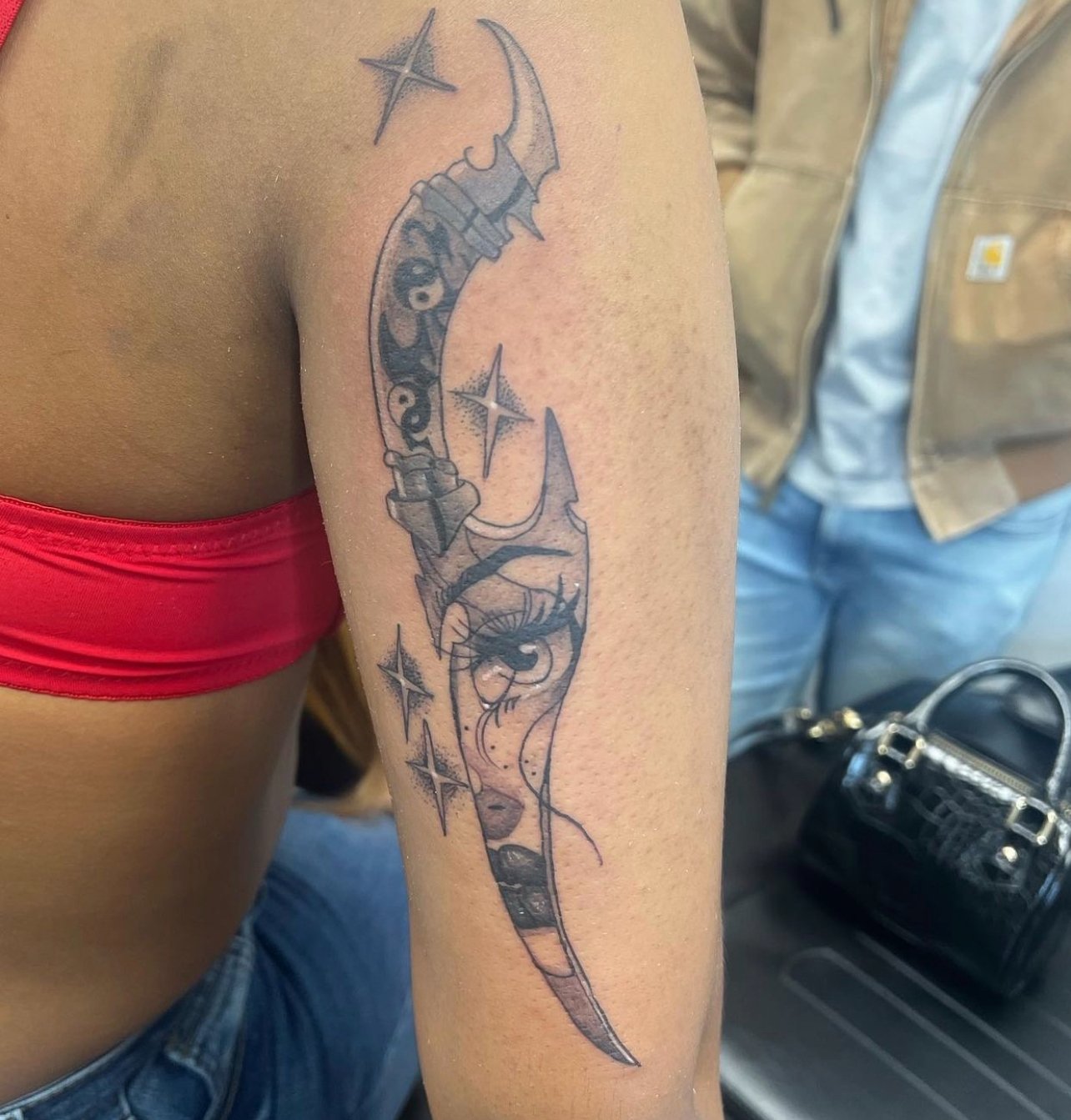 Tattoo of a stylized dagger with stars around it on a person's upper arm.