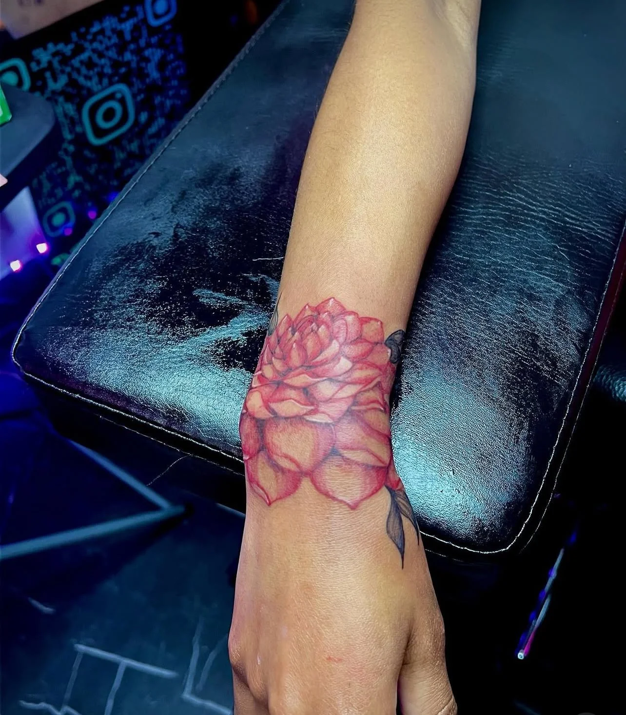 Colorful tattoo of a red and pink flower on a person's forearm.