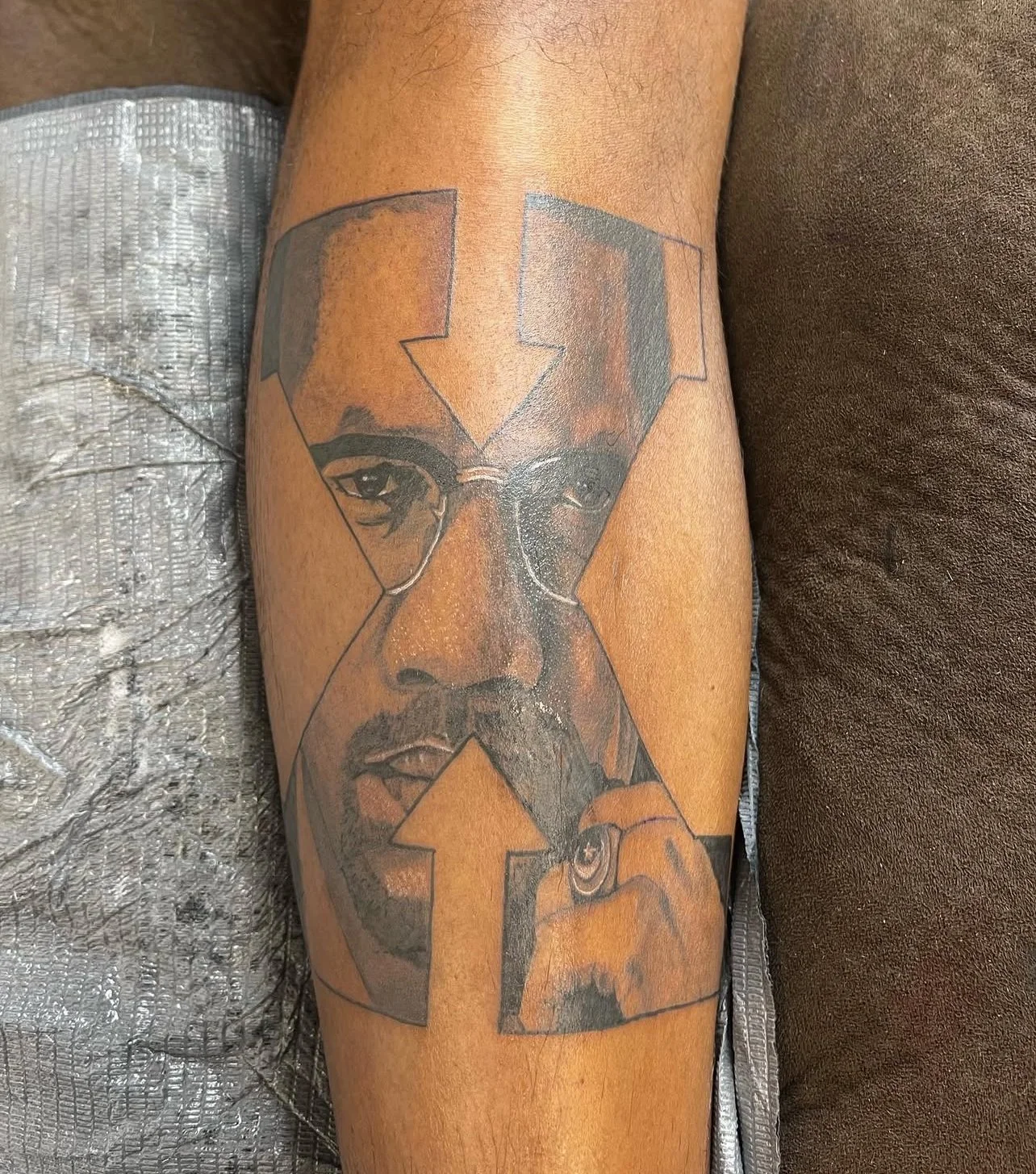 Tattoo of a man's face within four arrows forming a square, with two arrows pointing up and down, and the face holding a cigar. Tattoo of Malcolm X, a black panther activist.