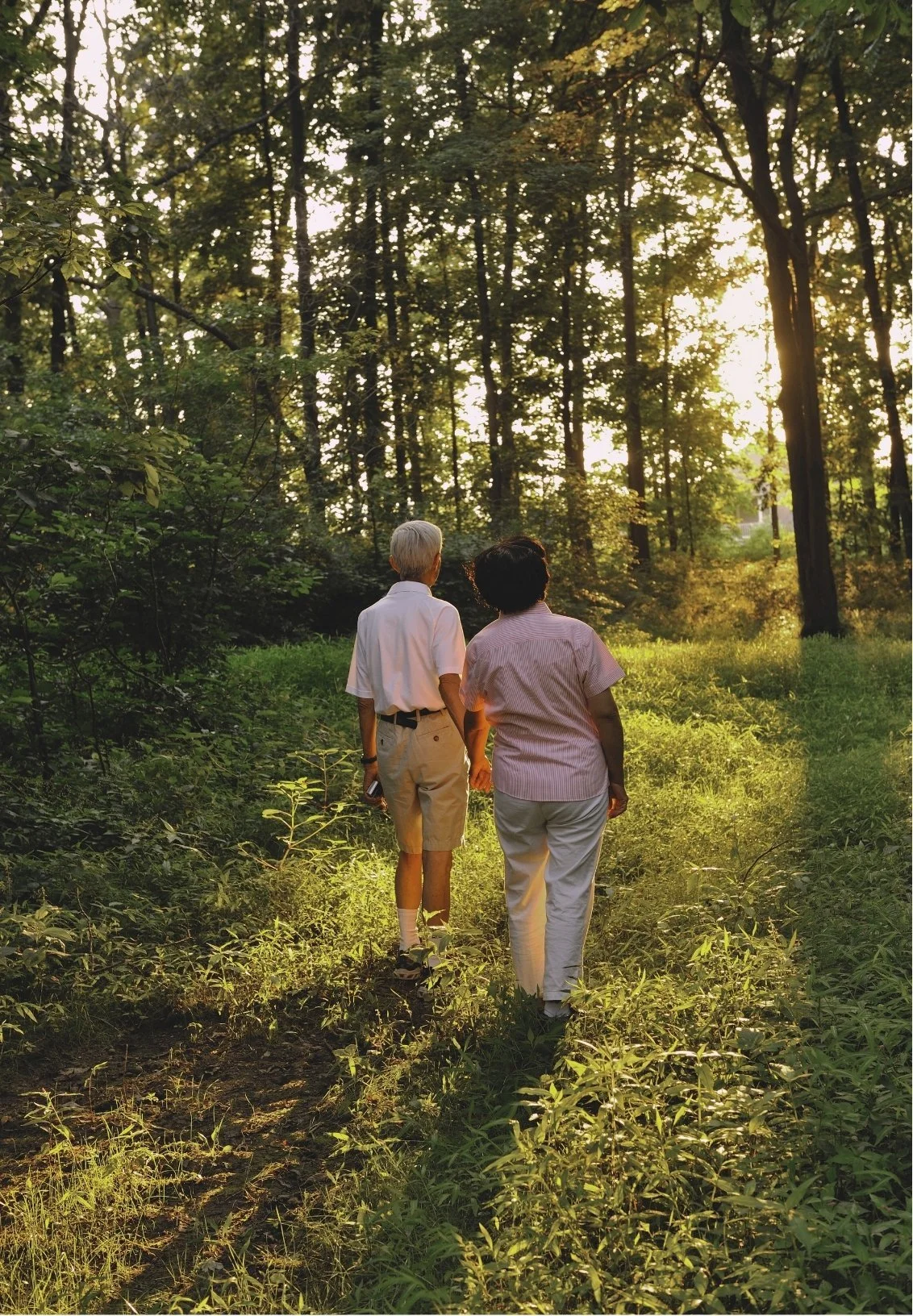 Two people walking side by side on wooded trail holding hands