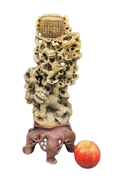 Carved wooden sculpture featuring various animals and a honeycomb pattern, placed on a reddish base, with an apple in front.