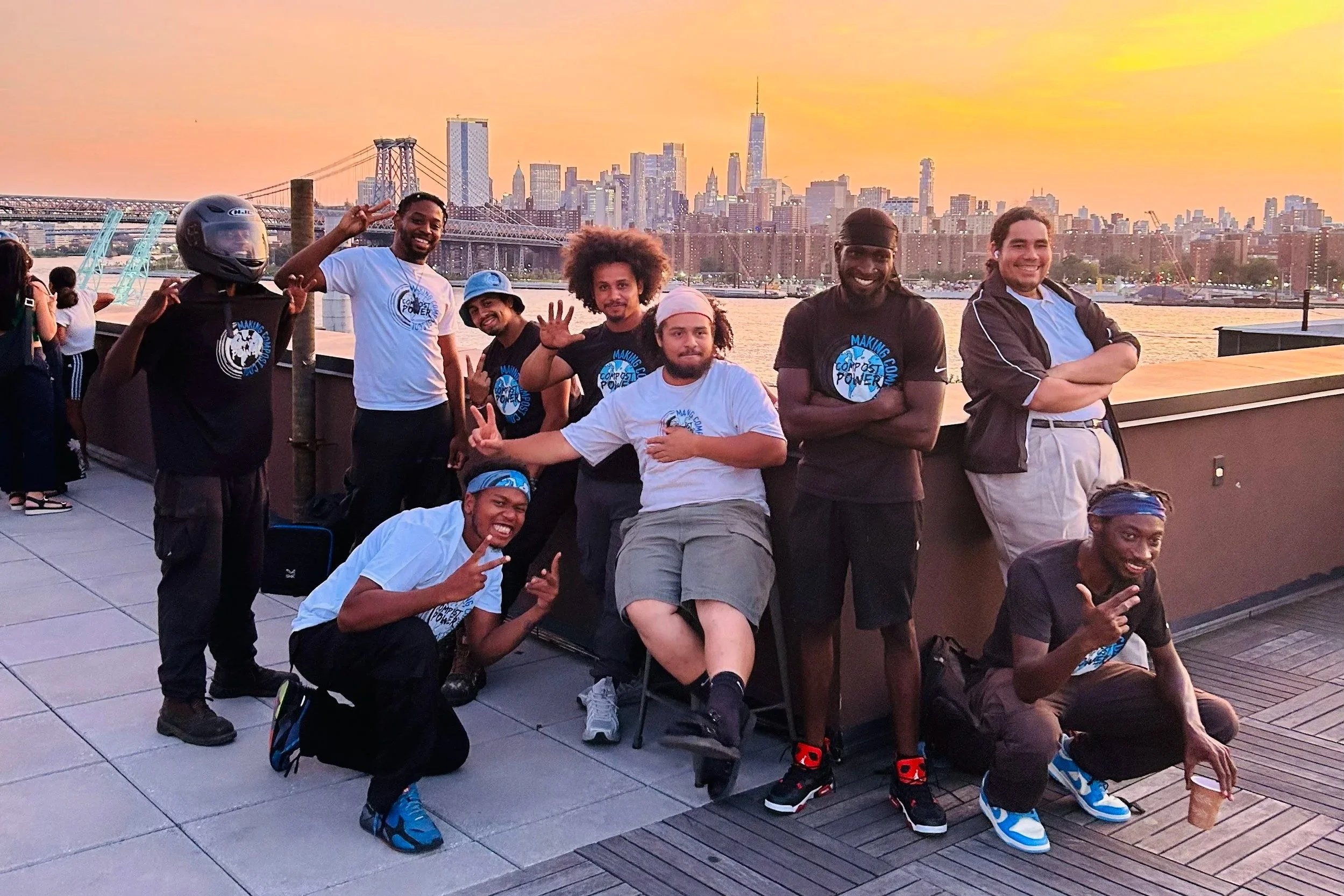 Compost Power team members posing together on a rooftop with city skyline and bridge in the background during sunset
