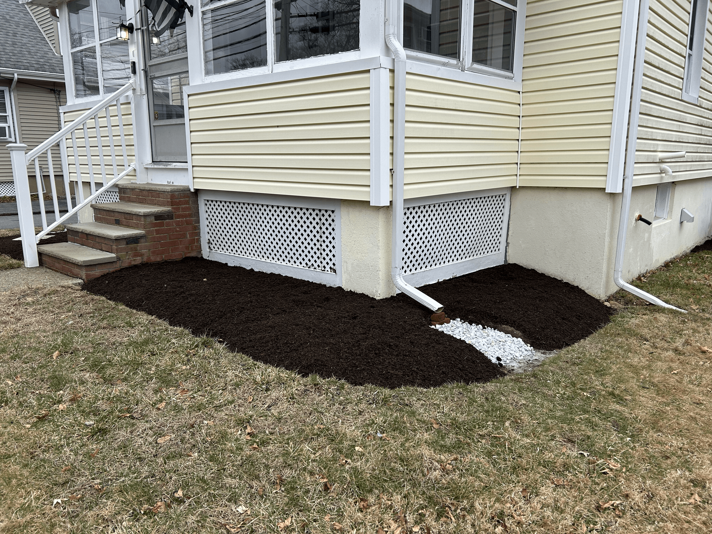 A house foundation with freshly tilled dark soil, gravel, and pipes, with stairs leading to a porch on the left side.