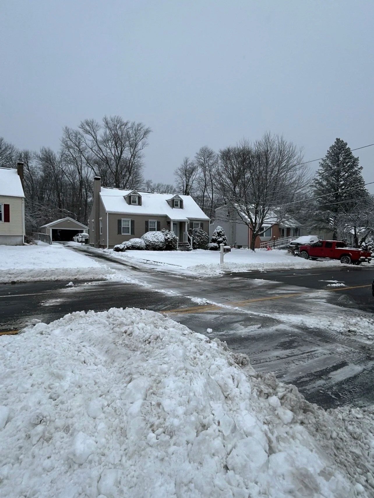 Snow-covered suburban neighborhood with houses, trees, and a parking lot.