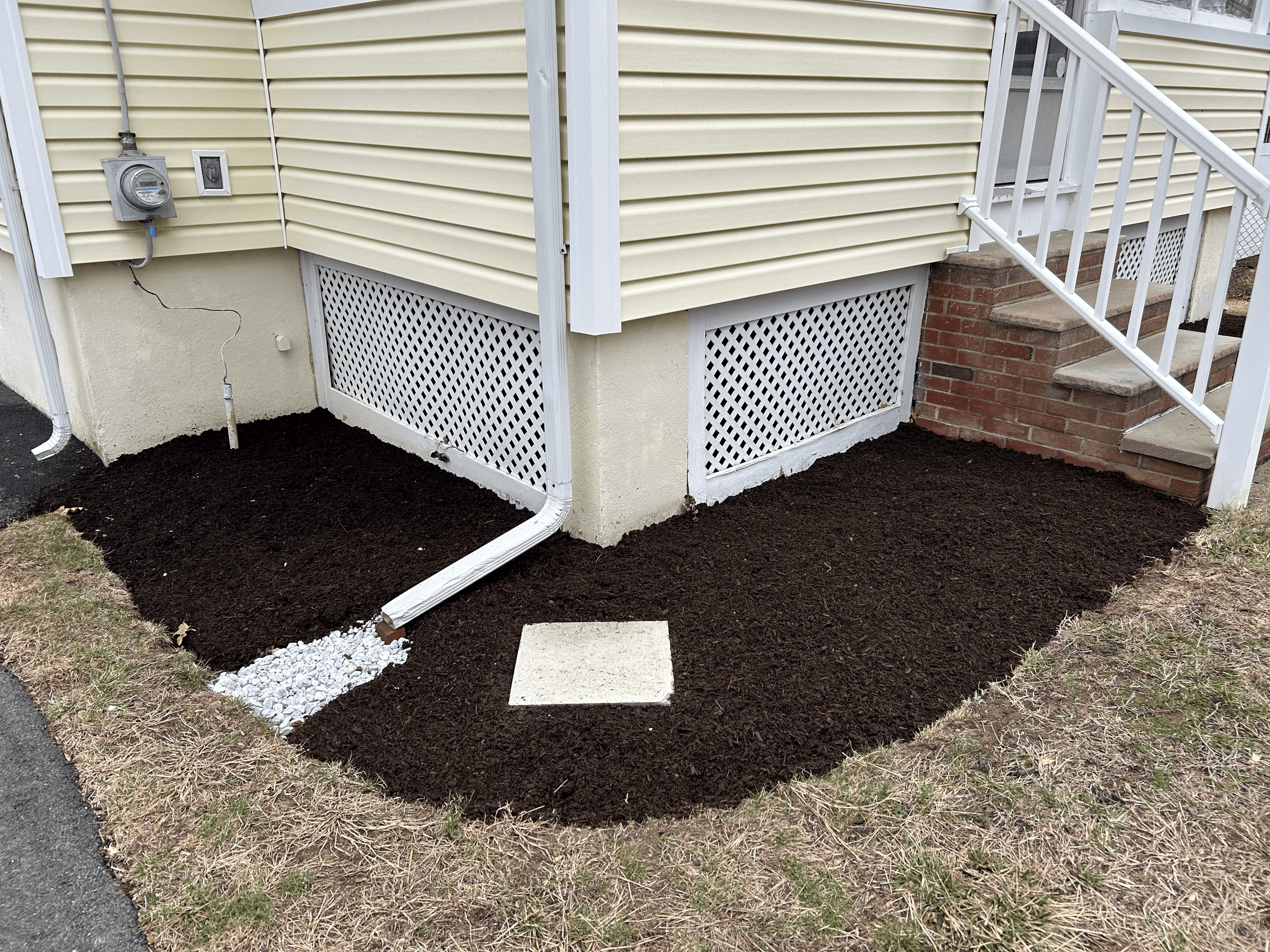 Freshly landscaped soil around the foundation of a house with stairs, gutters, and a vented lattice skirt.