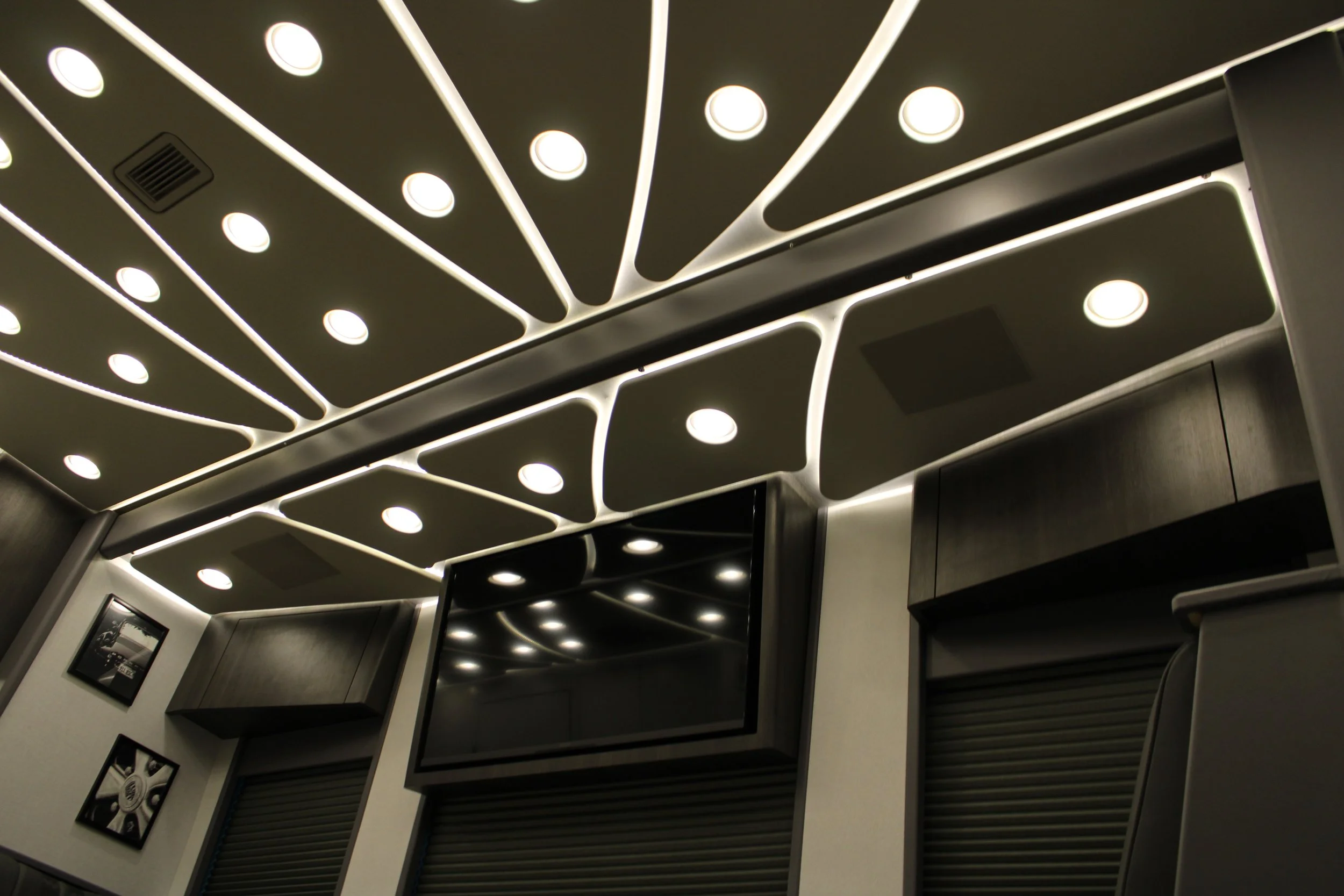 Modern ceiling with LED lights and black cabinets below a large flat screen tv in a contemporary room.