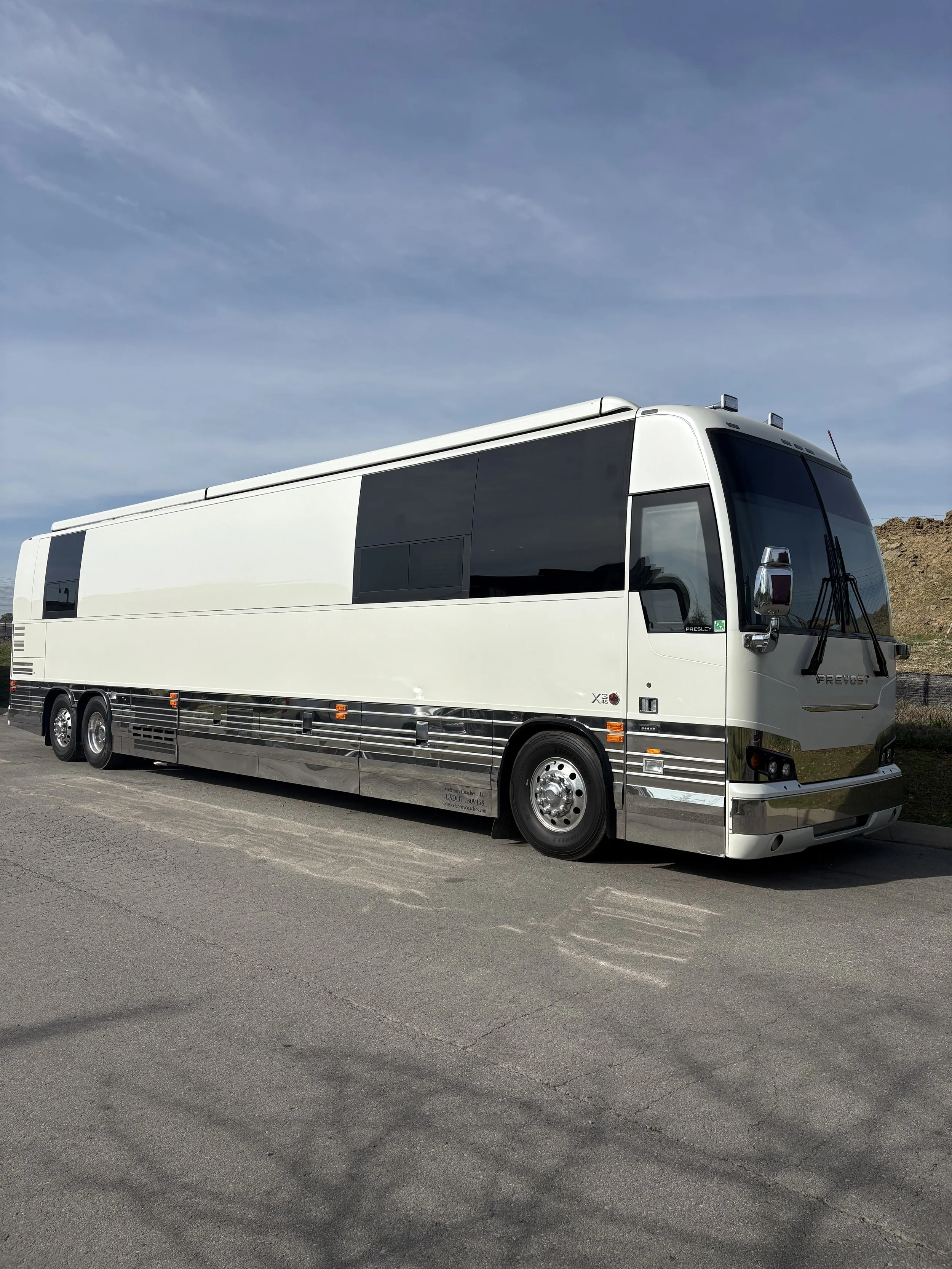 A large white tour bus parked on a paved road with a clear blue sky overhead.