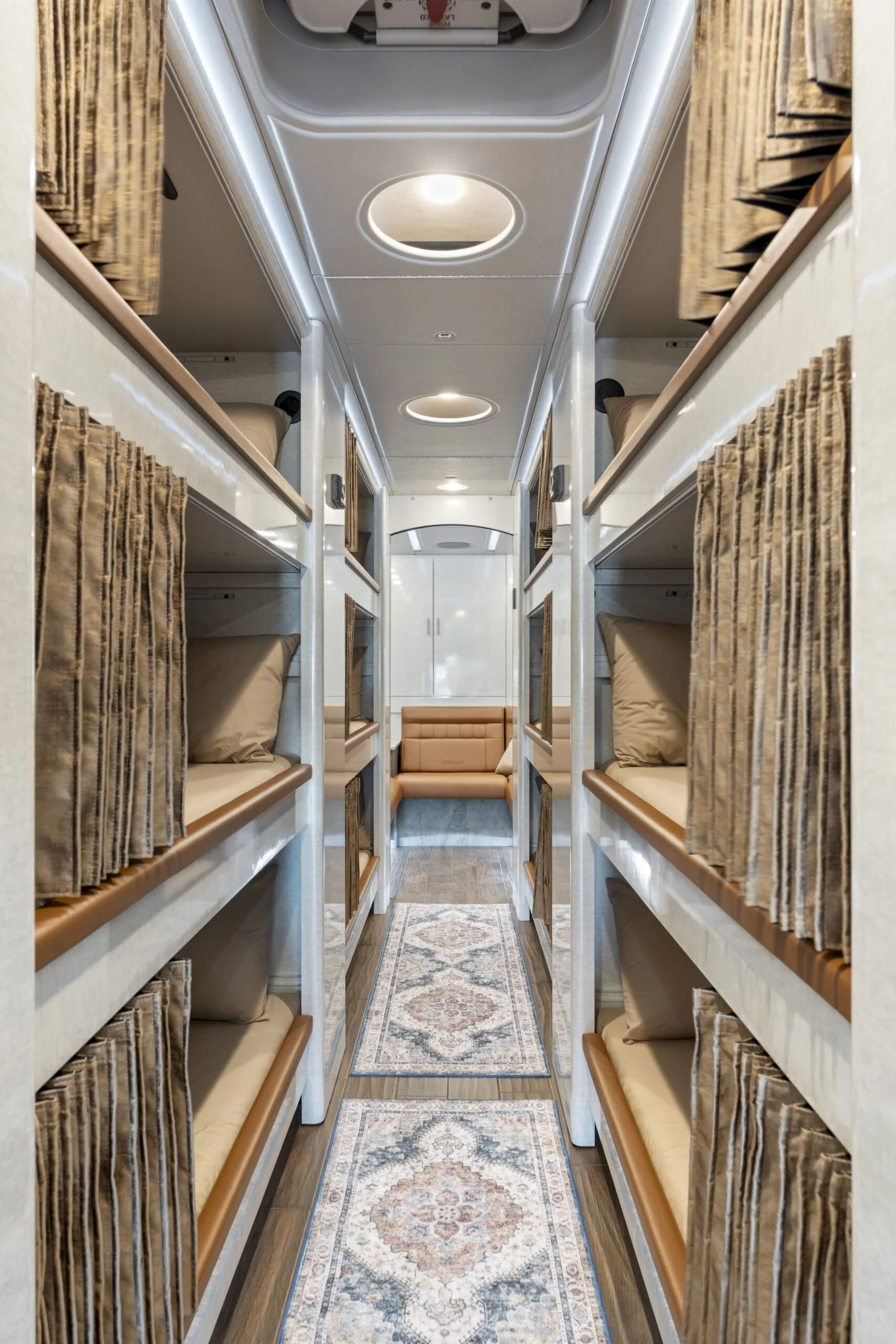 Inside of a modern airplane's sleeping quarters with stacked beds on both sides, small pillows, curtains for privacy, ceiling lights, and a carpeted aisle leading to a seating area
