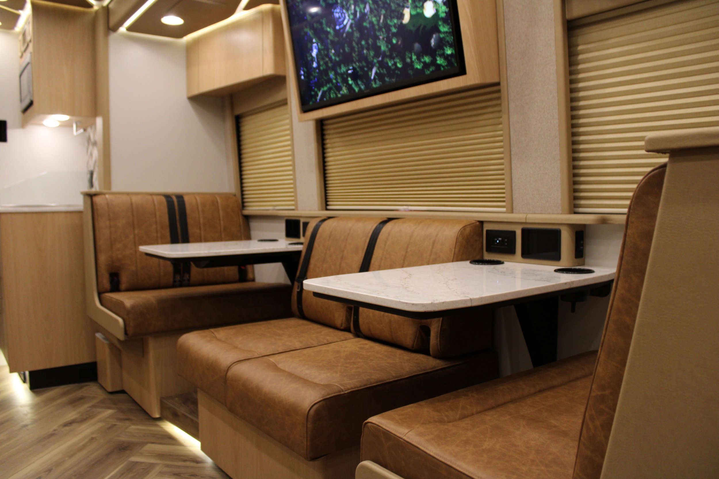 Interior of a modern recreational vehicle or camper with leather booths, marble tables, window shades, and a television