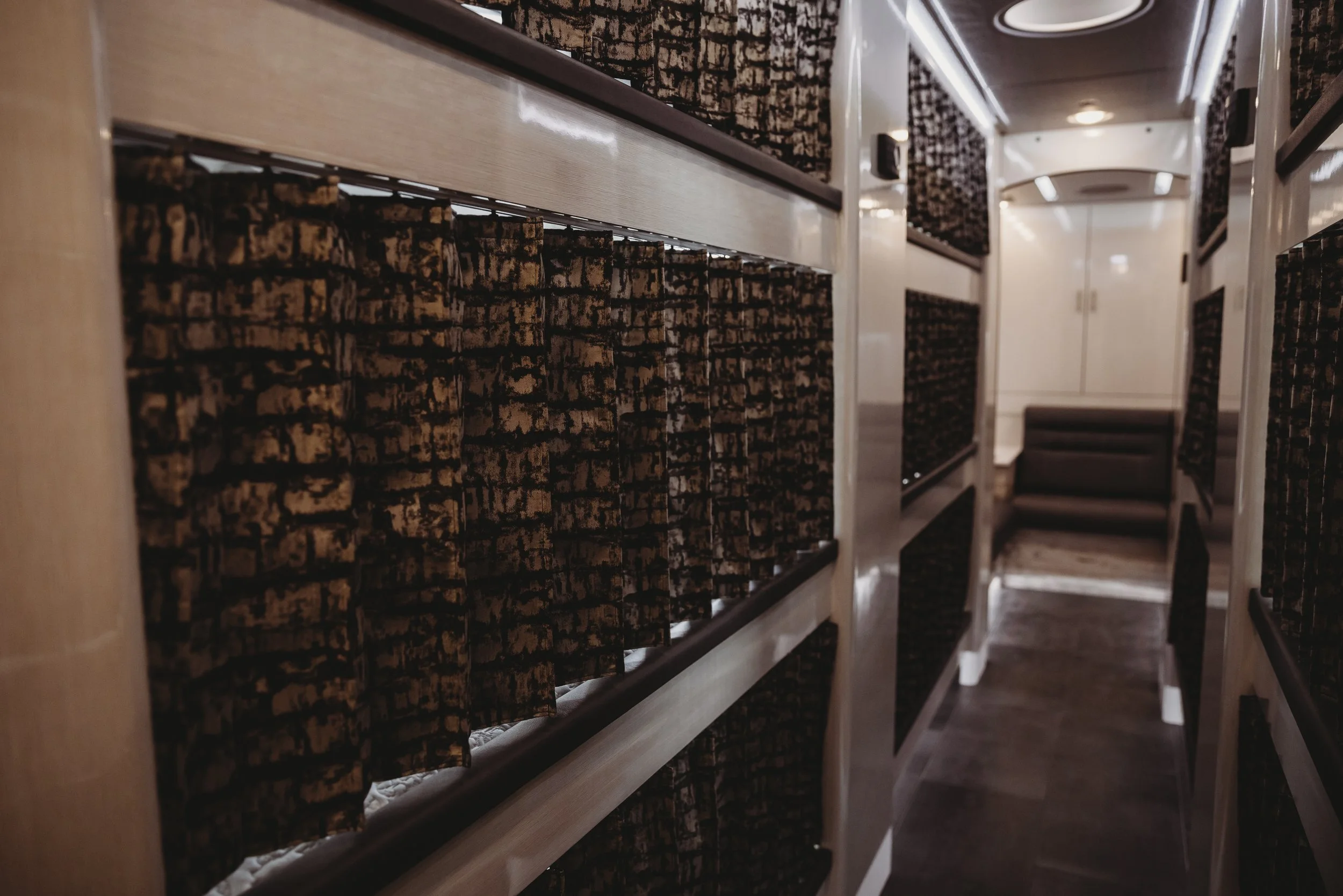 A narrow corridor with shelves on either side filled with black and brown patterned fabric or clothing items, leading to a door at the end.