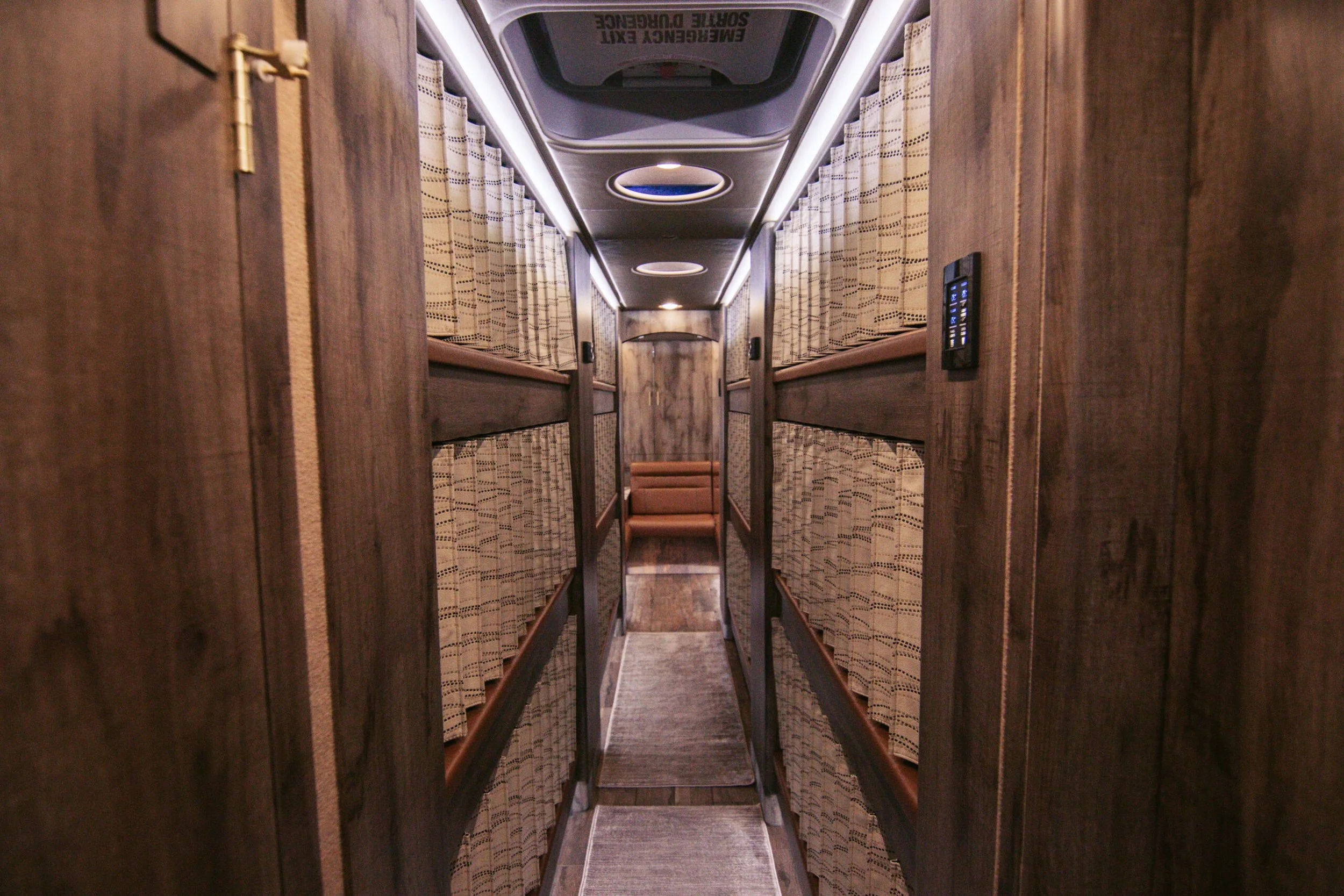 View of a cozy, well-lit narrow corridor inside a train with two sets of bunks on each side, curtains for privacy, and a small set of stairs at the end.