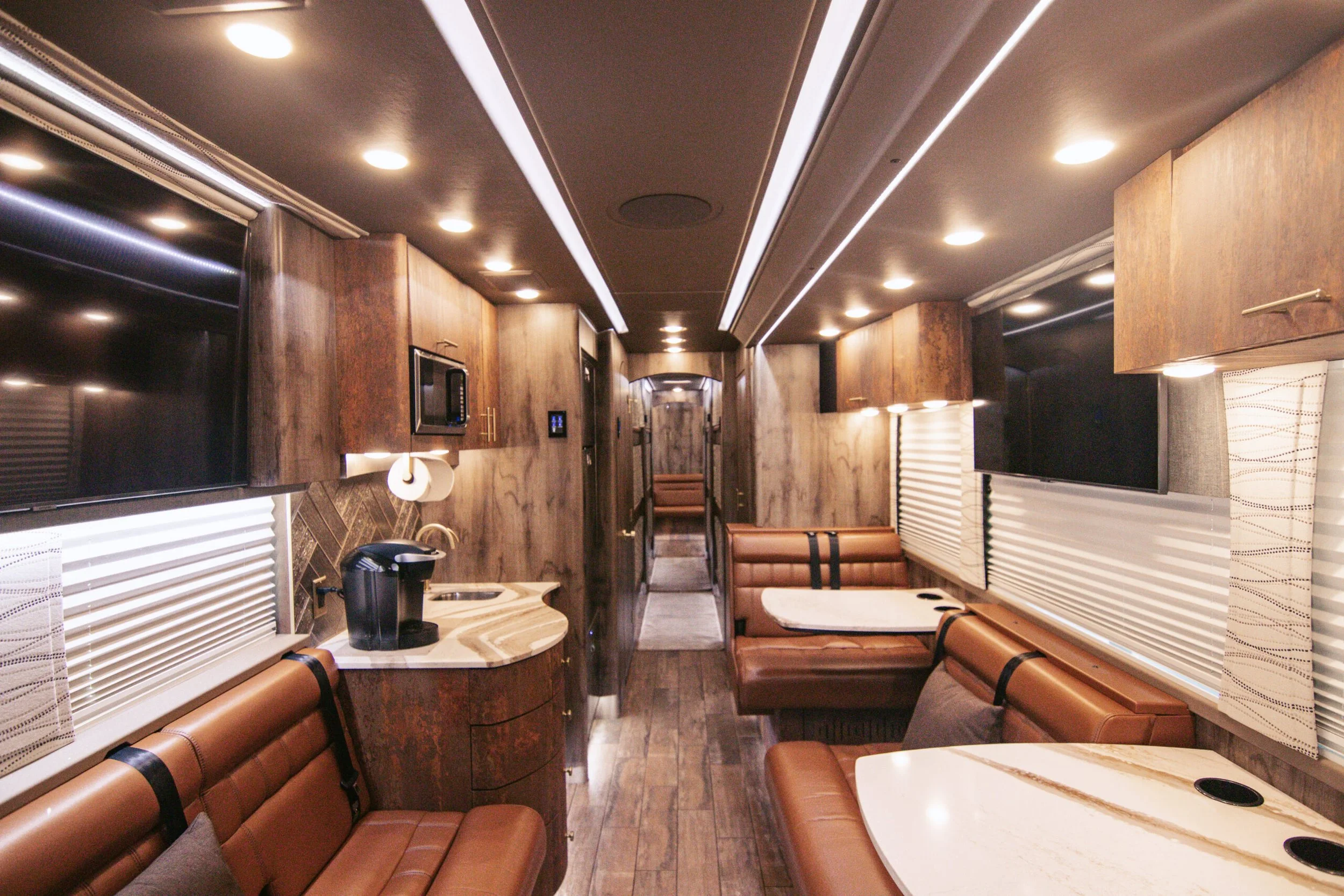 Interior of a recreational vehicle with leather booths, microwave, coffee maker, and large windows with blinds.