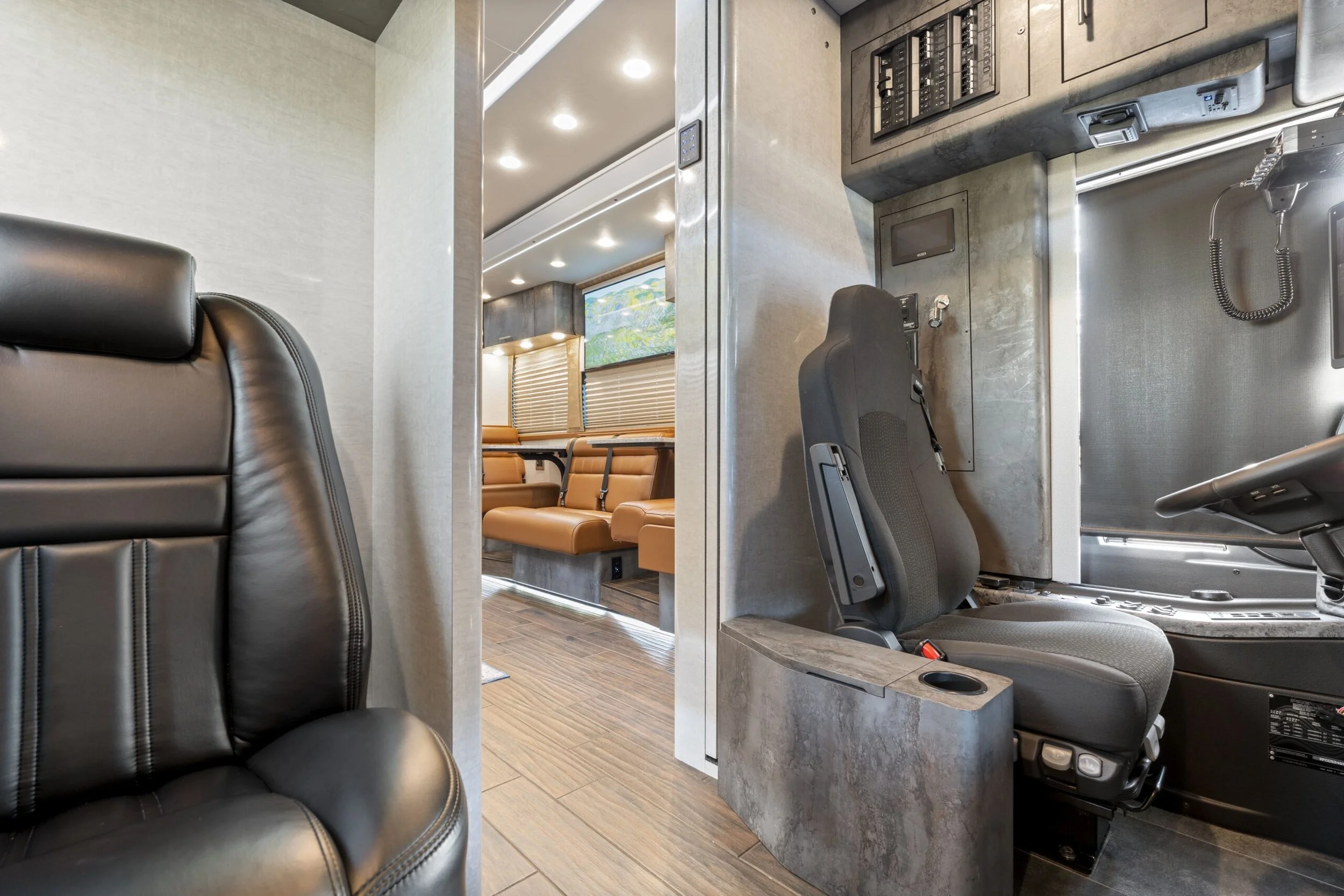 Interior of a bus showing a leather seat on the left, a driver's seat and control panel on the right, and a row of tan seats in the background.