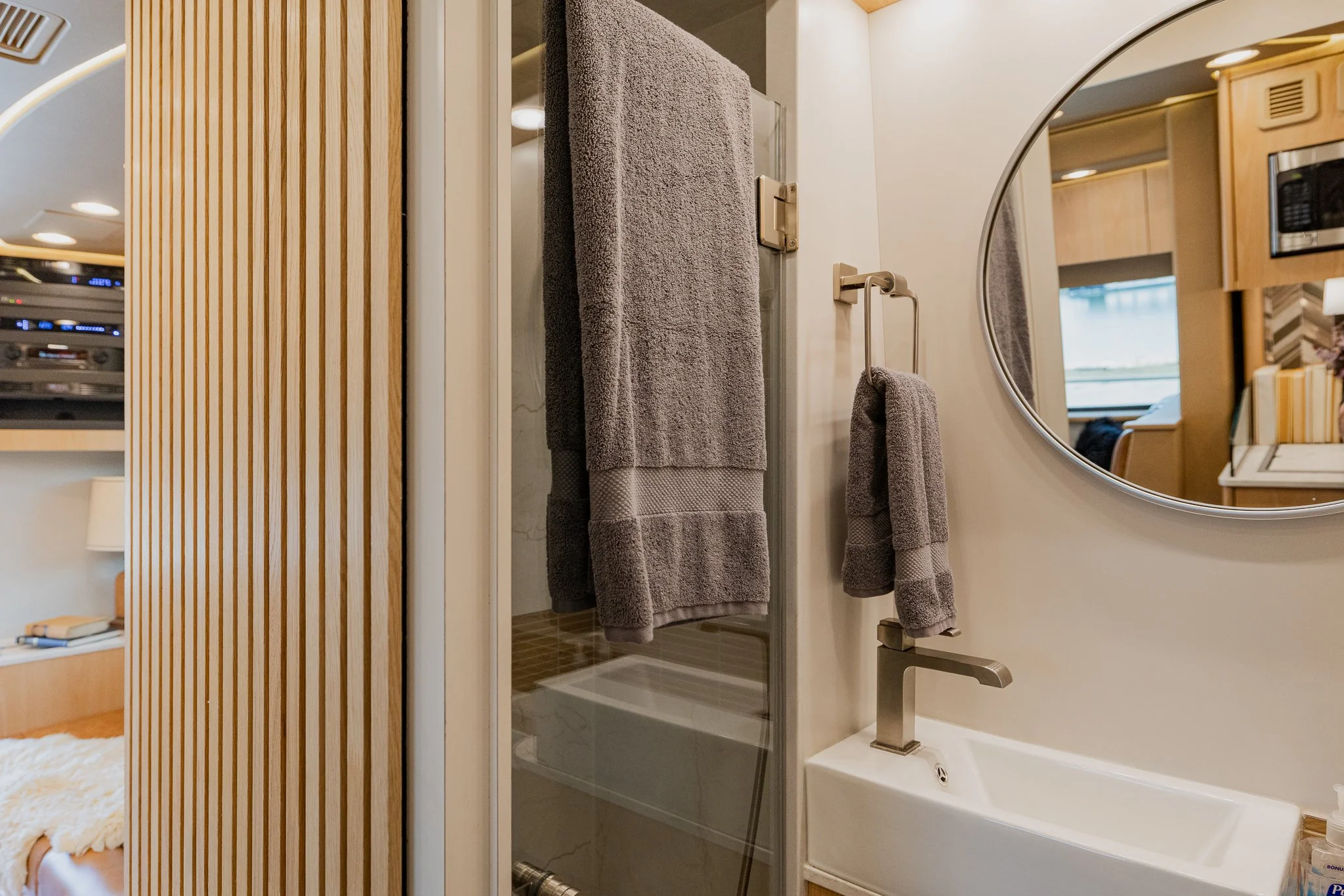 A small bathroom with a mirror, sink, gray towels, and a shower with a glass door.