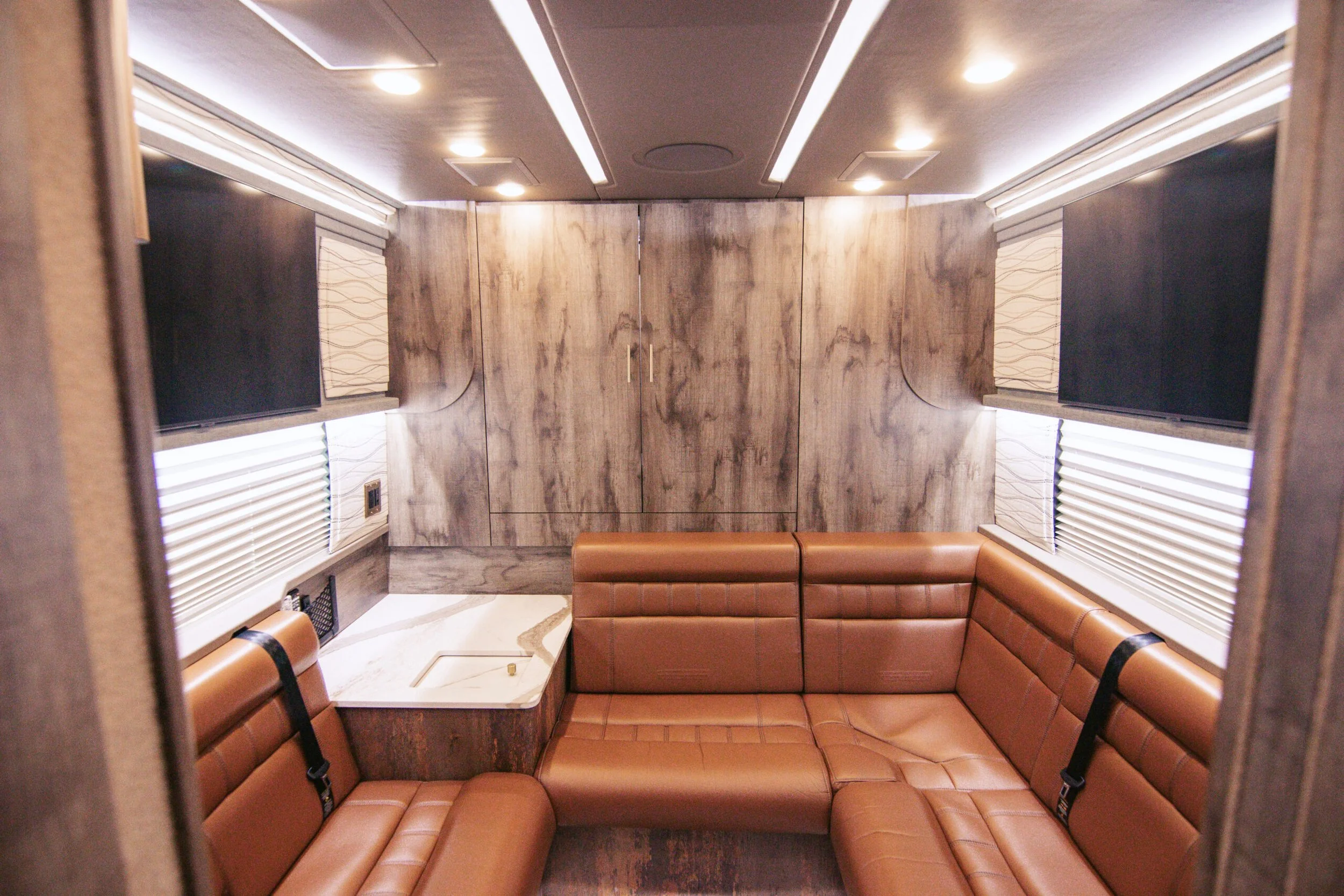 Interior of a lounge or office featuring leather sectional seating, wood panel walls, windows with blinds, and ceiling lights.