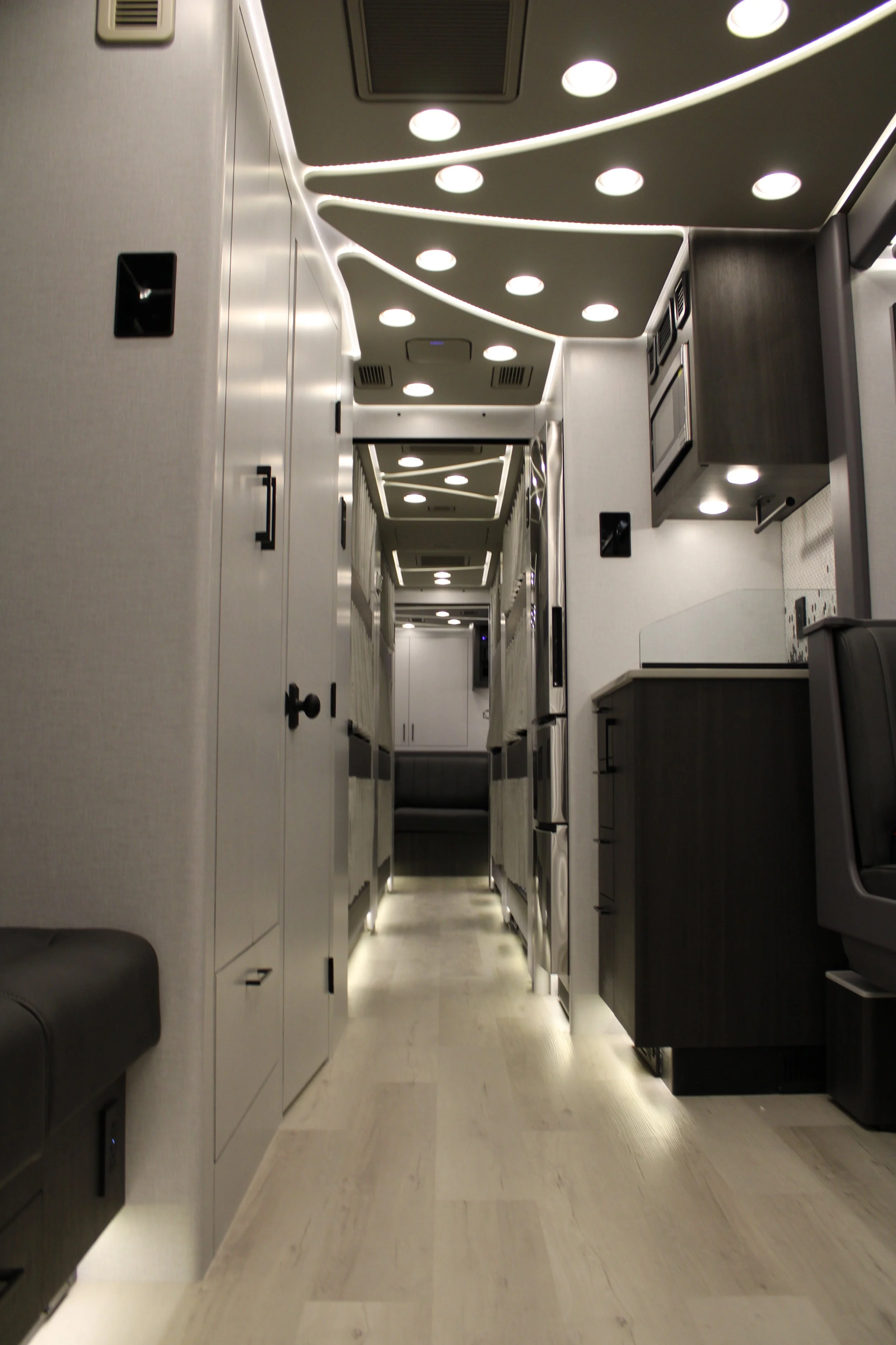 Interior of a modern private jet cabin showing a corridor with overhead lighting, cabinetry, and seating area.