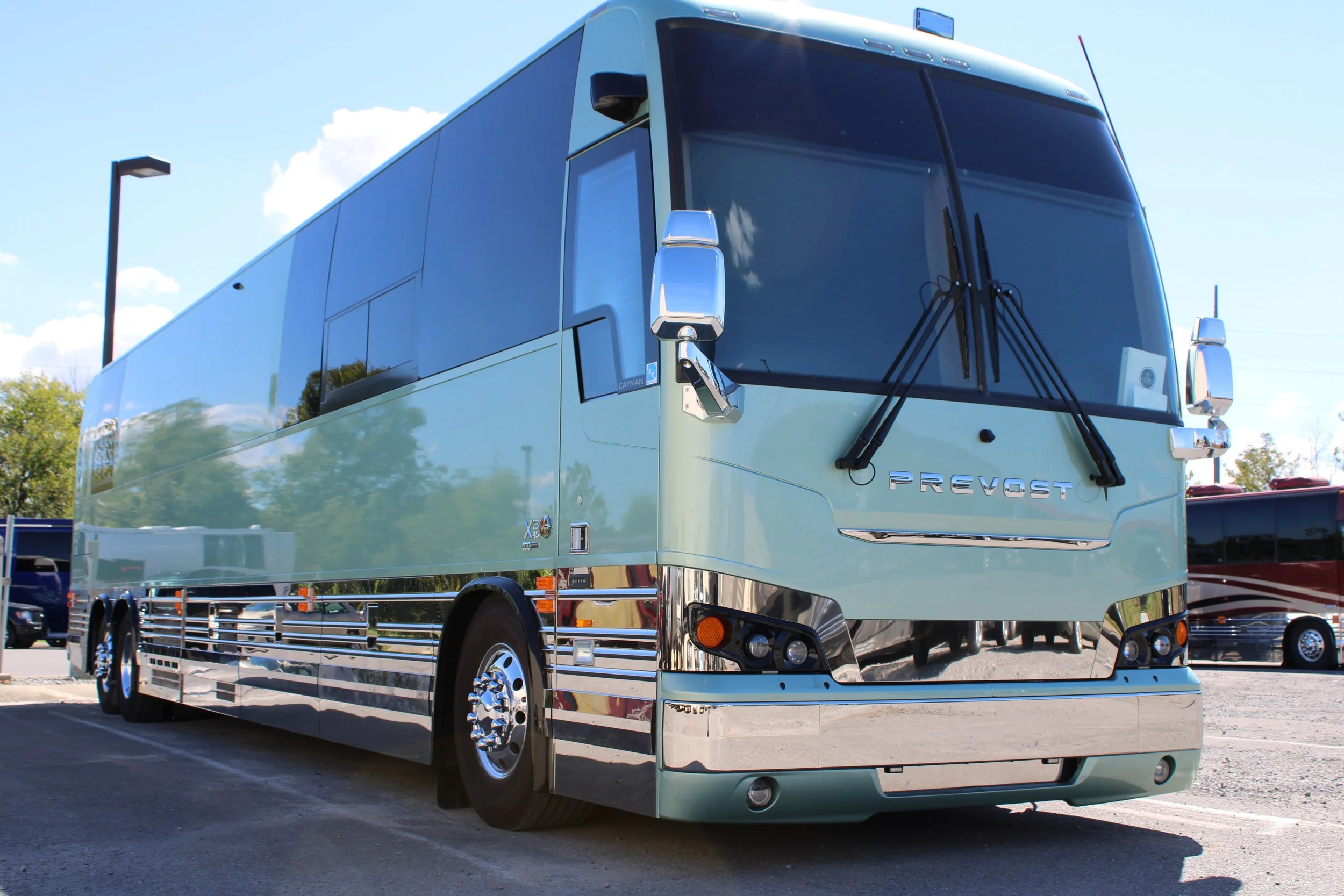Silver Prevost bus parked on a parking lot with a blue sky background.