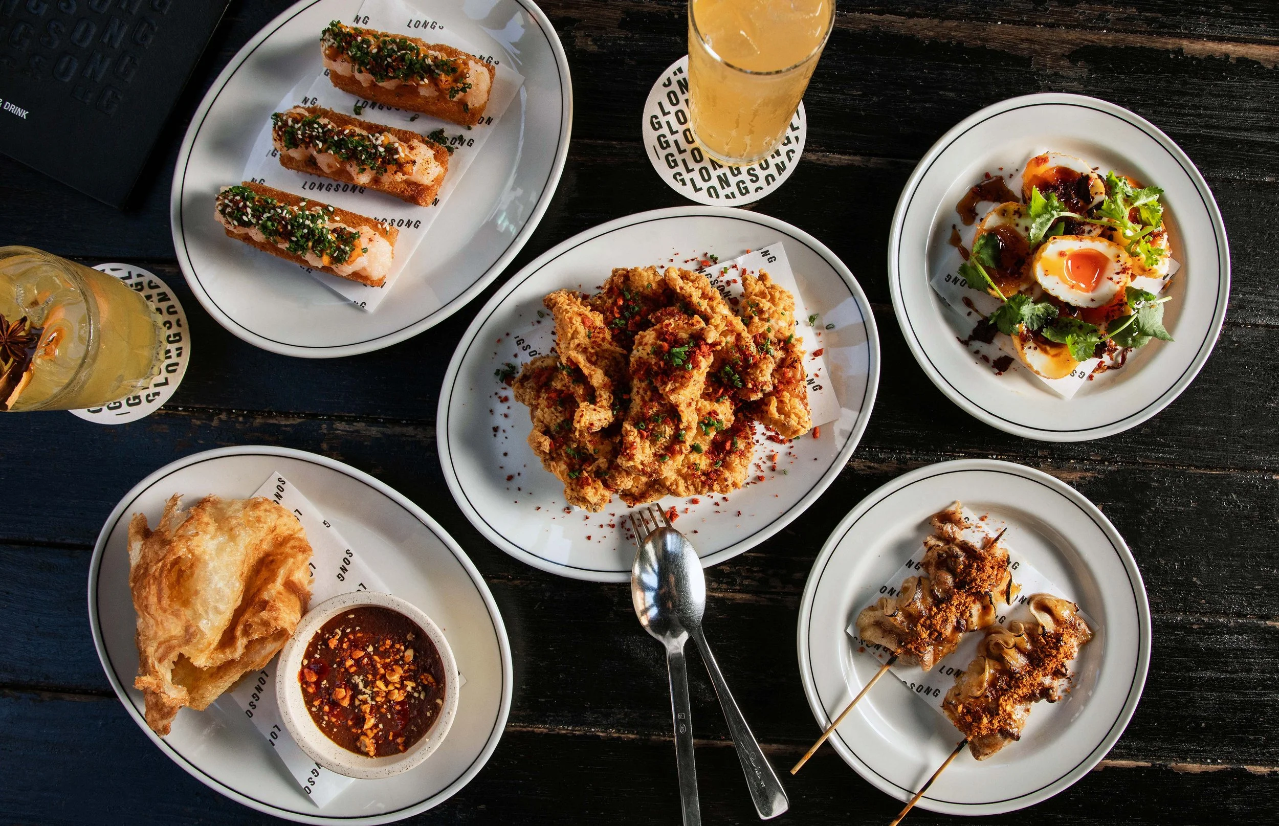 Various Longsong dishes served on white plates on a dark wooden table.
