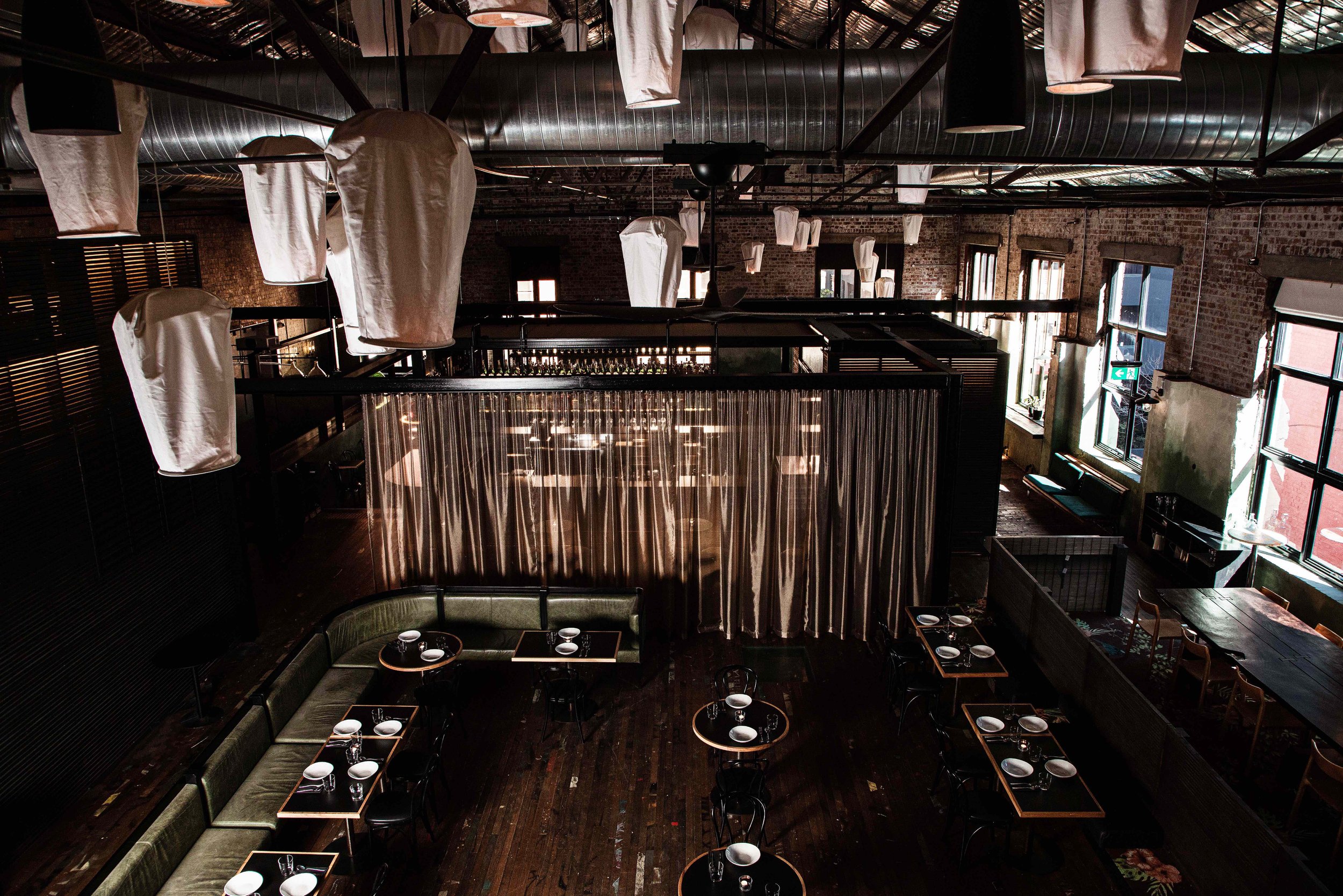Interior of Longsong with tables set for dining, large windows allowing natural light, exposed brick walls, and hanging lantern decorations.