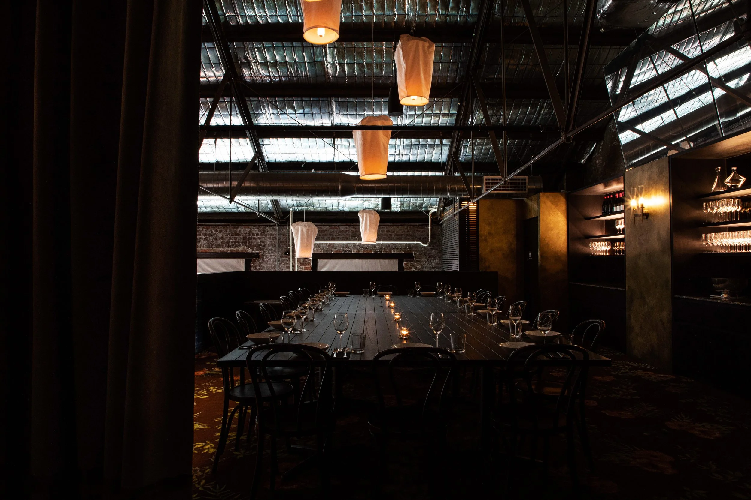 A dimly lit private dining room at Longsong with a long rectangular table set with wine glasses, plates, and candles, surrounded by black chairs.