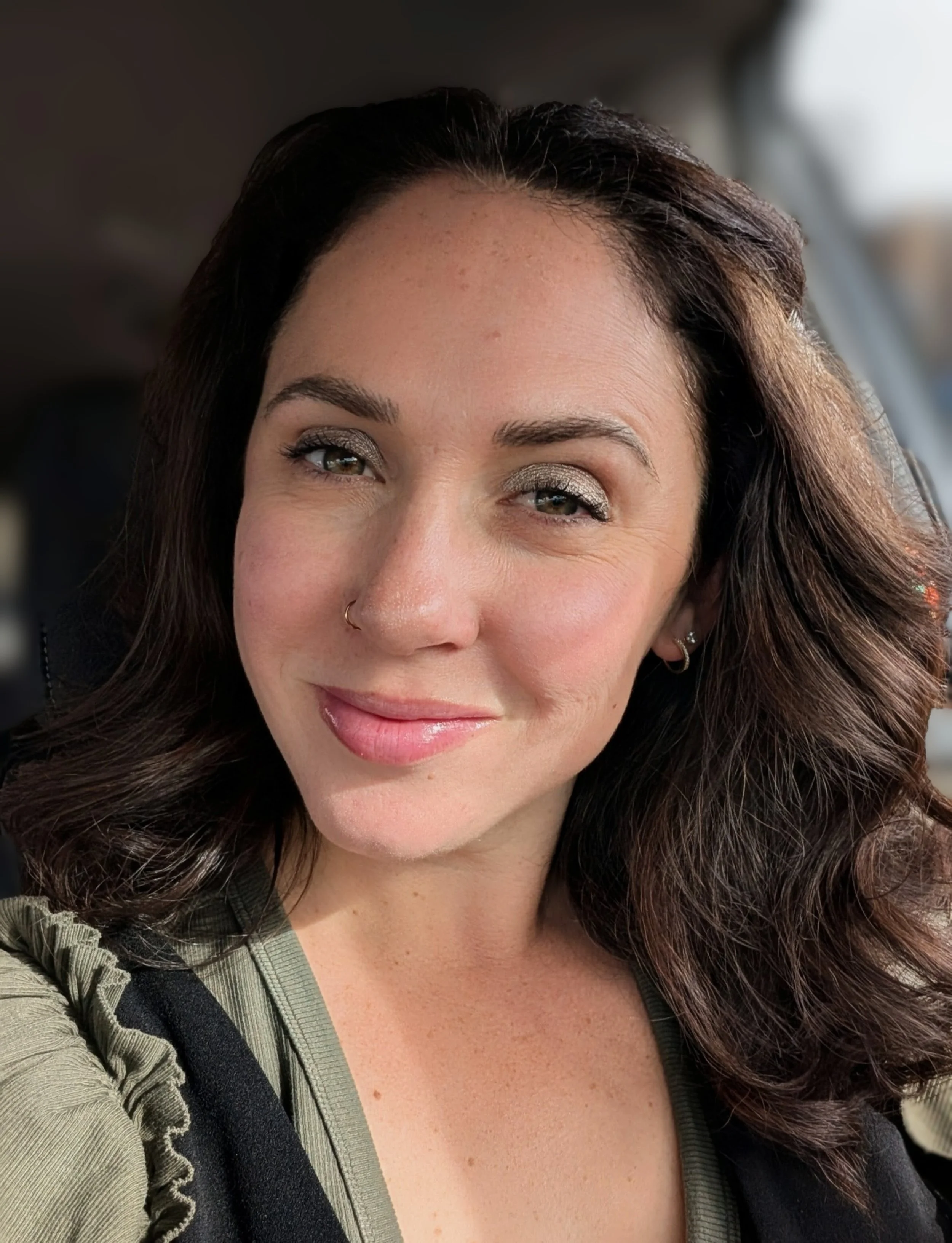 Photo of Katie Ludlow Rich in warm lighting, wearing an olive green ruffle shirt and black jumper.
