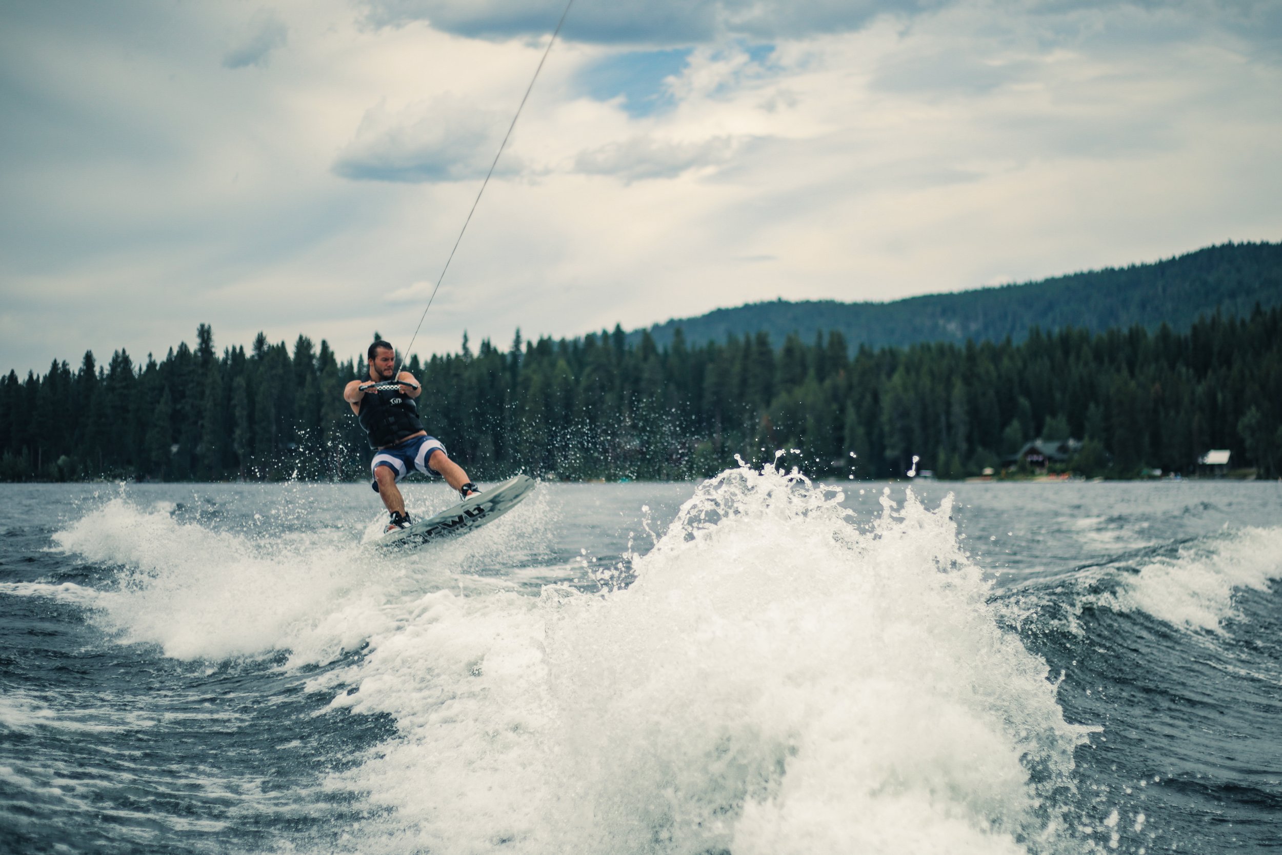 Man wakeboarding on Lake Payette with a beautiful forest and mountains in the background.
