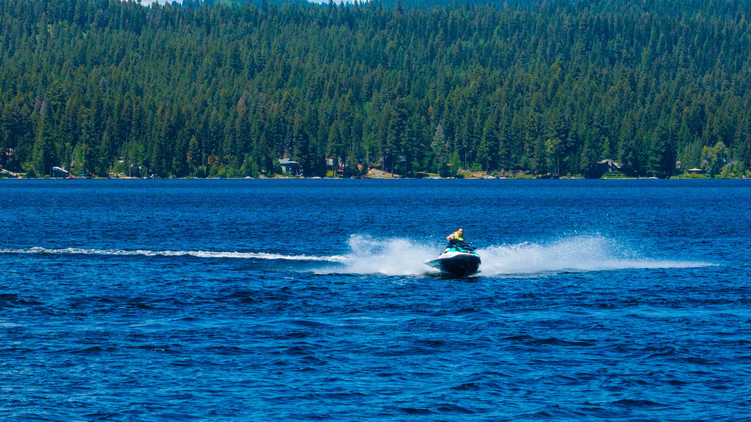 Man jetskiing on Lake Payette with a beautiful forest and mountains in the background.